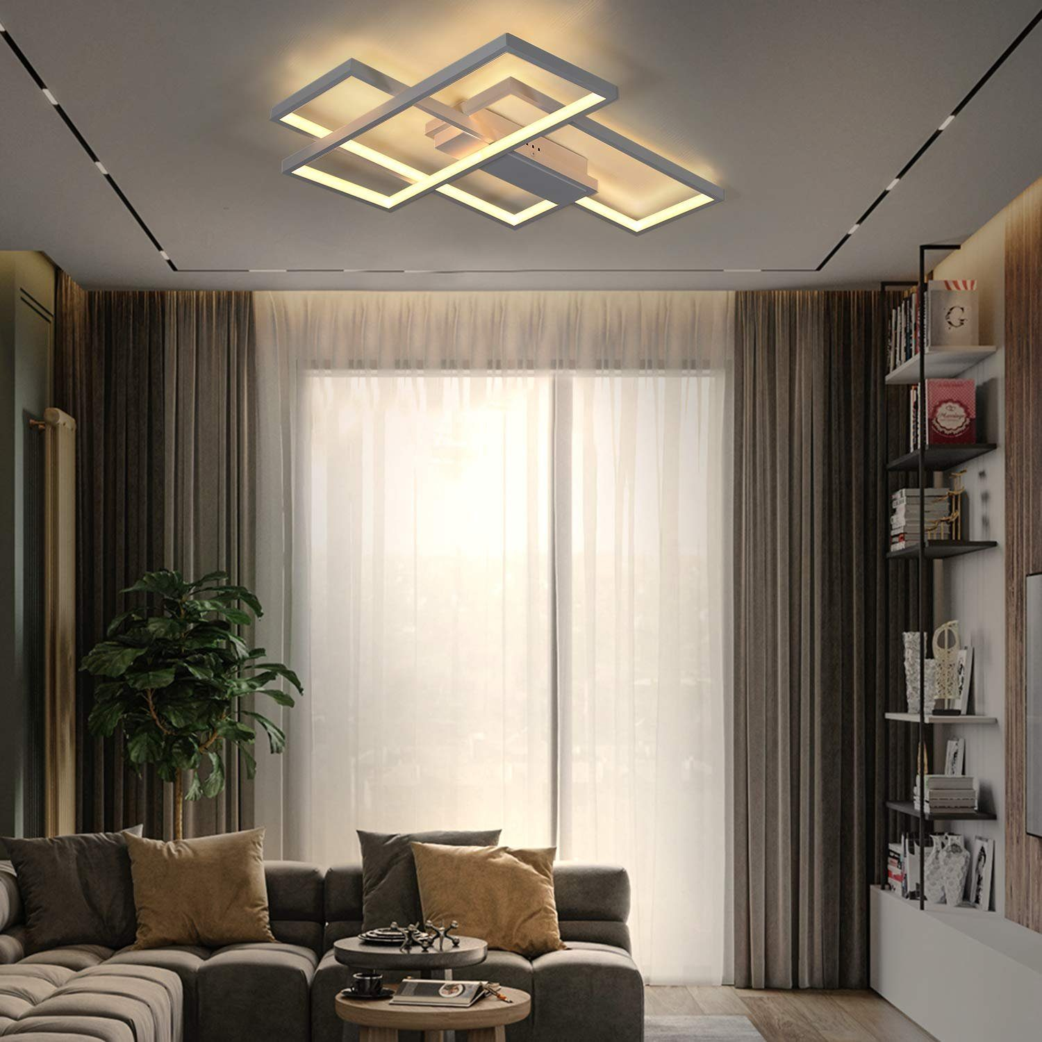 Nowoczesny salon z szarą sofą, dużym oknem i geometryczną lampą sufitową. Widoczna jest również roślina i regały.