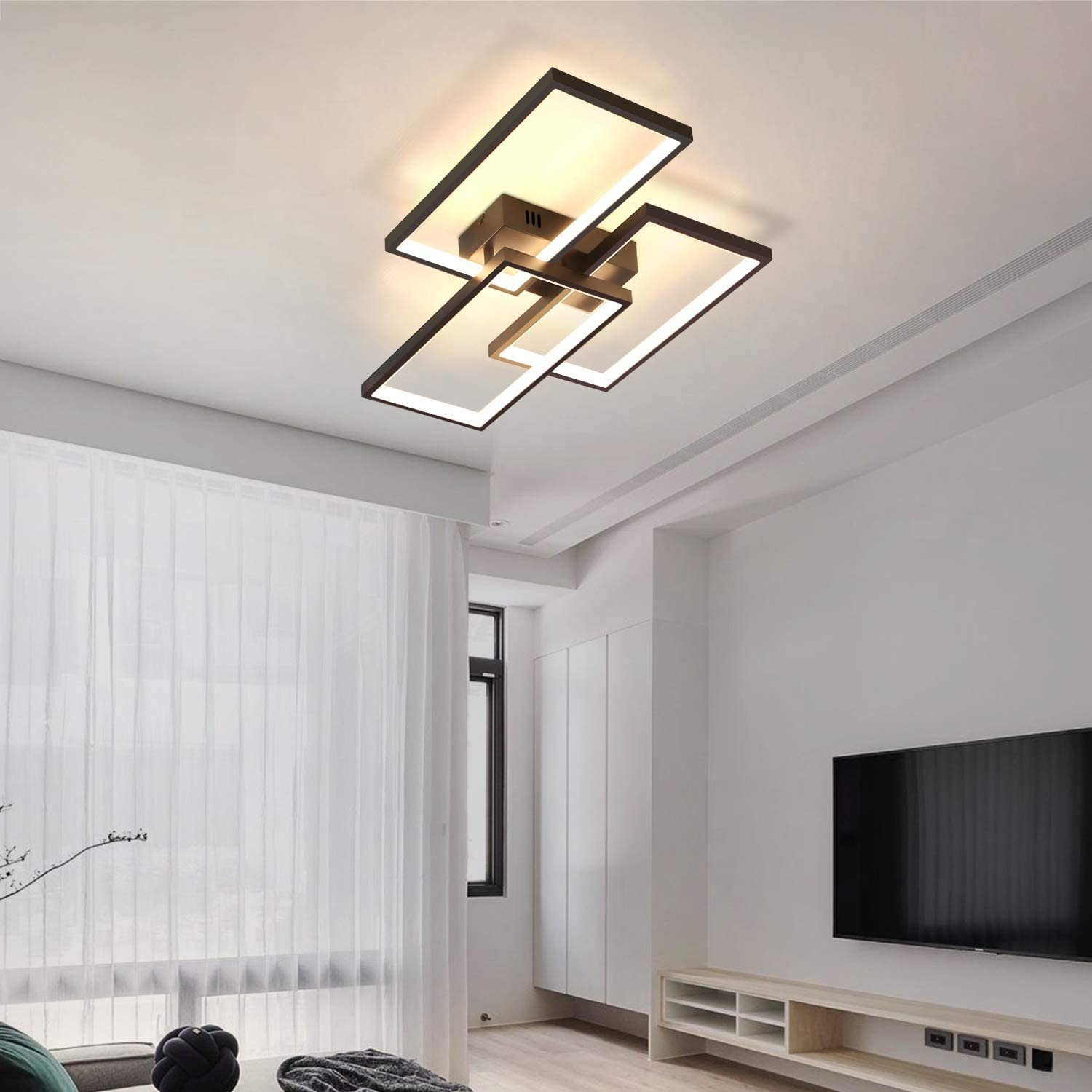 Un moderno soggiorno con una lampada da soffitto geometrica. C'è una TV, tende bianche e un mobile basso.