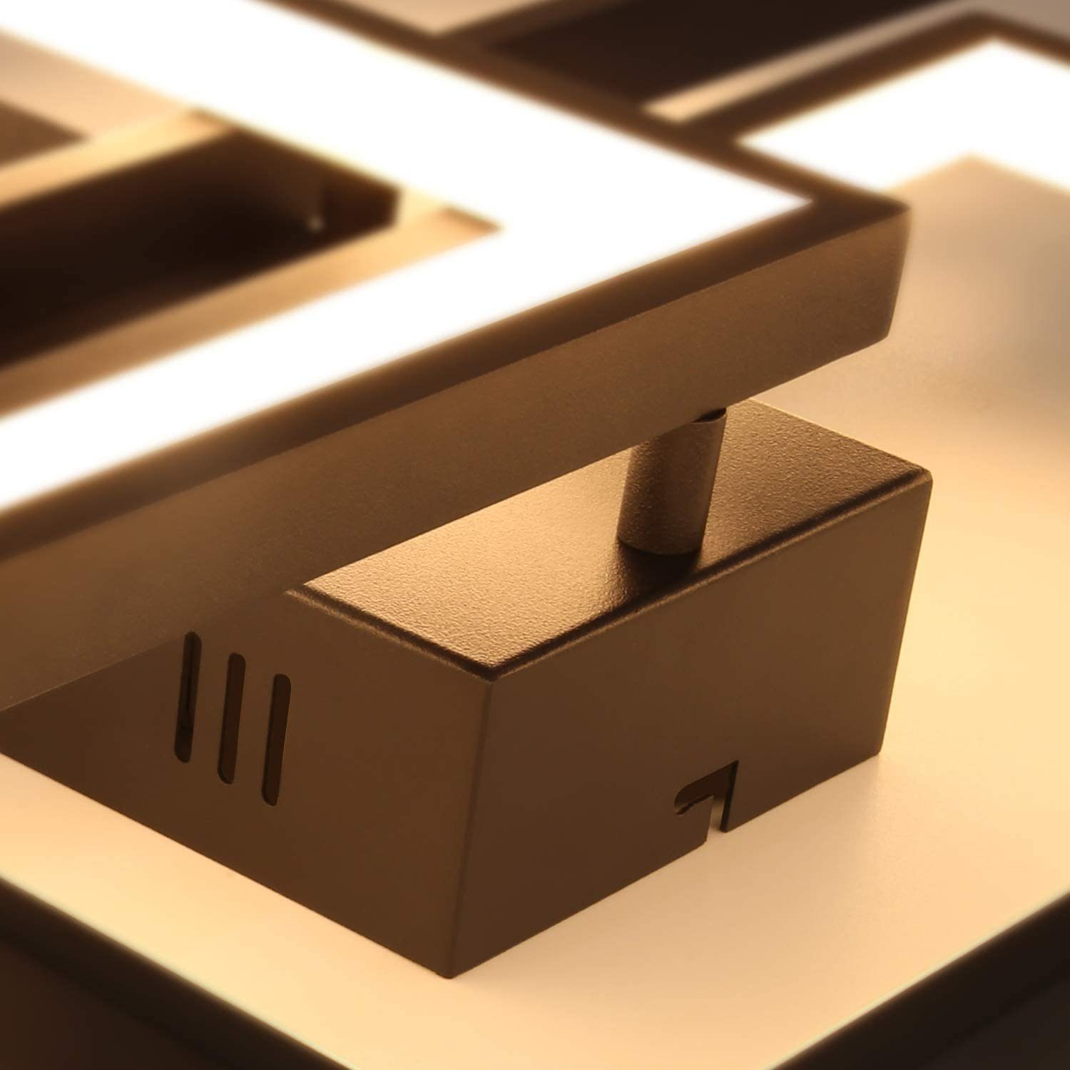 Primo piano di un apparecchio di illuminazione geometrico marrone. Presenta tre fessure verticali e un intaglio. Sono visibili luci bianche brillanti.