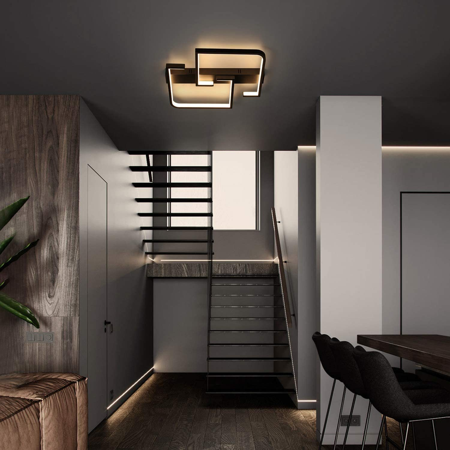 Scatto interno di una casa moderna con scale, pavimenti in legno e un'elegante lampada a soffitto. Sedie e un tavolo a destra.