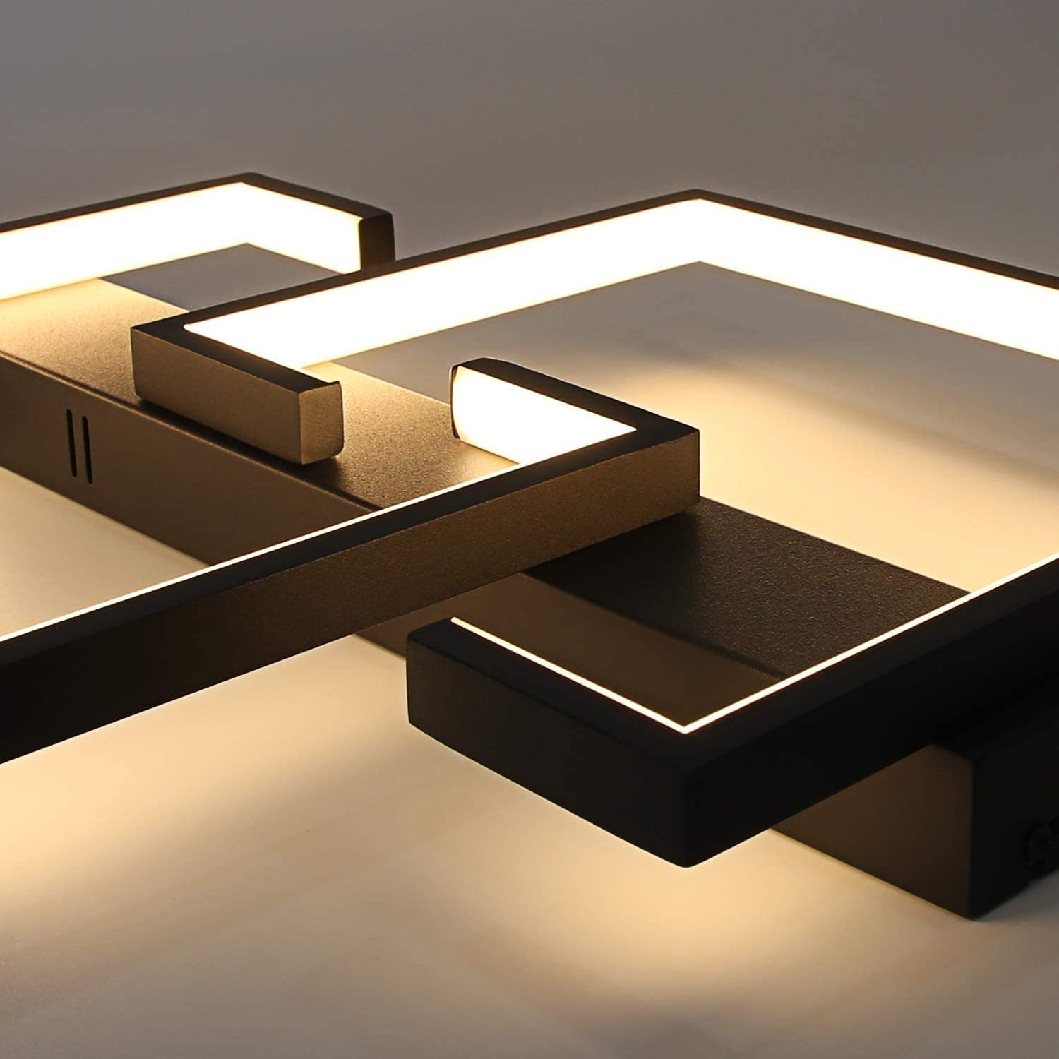 Un moderno apparecchio di illuminazione a soffitto in bianco e nero. Ha forme geometriche e linee illuminate, che proiettano luce soffusa.