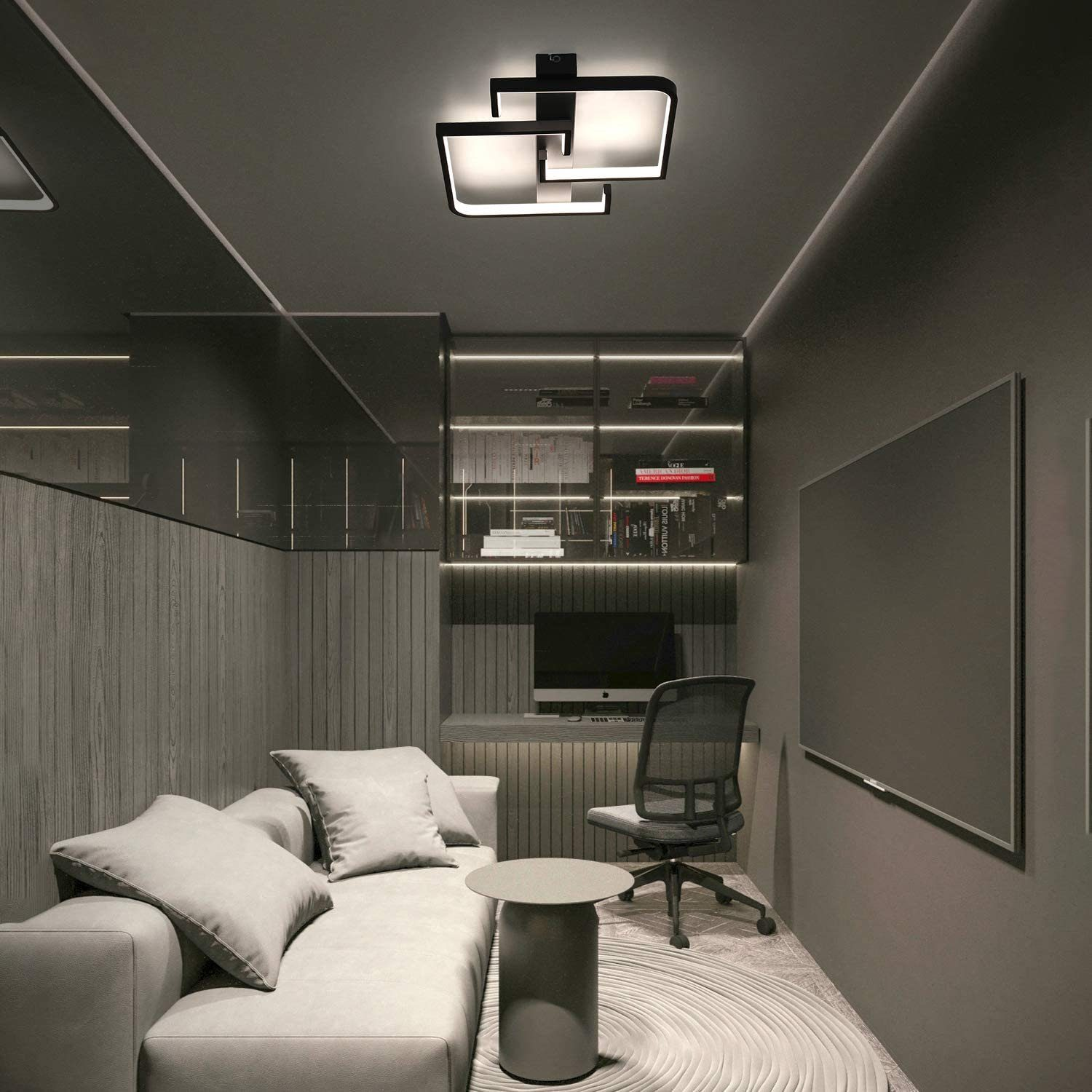 Un moderno spazio ufficio con divano grigio, scrivania, sedia e un'esclusiva lampada da soffitto. Sono visibili librerie e un grande schermo.