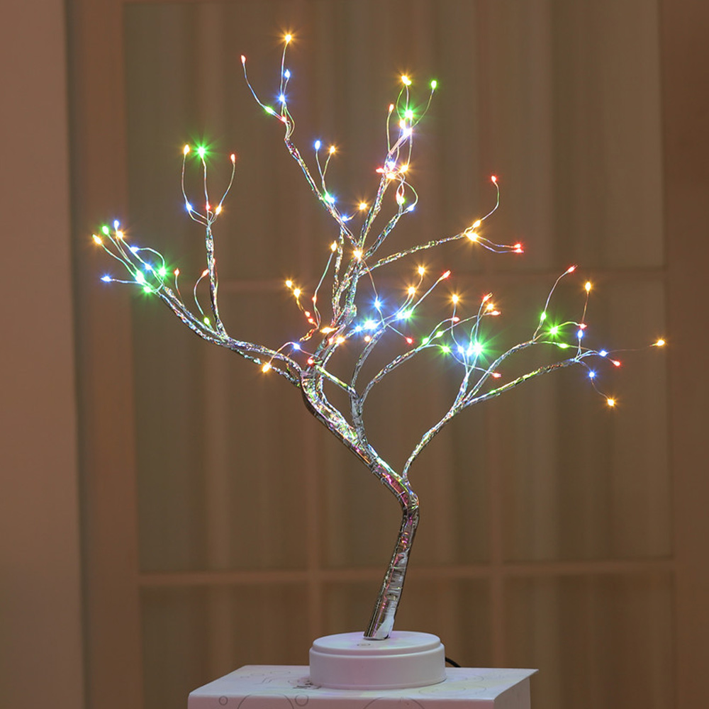 Ein dekorativer Baum mit silbernen Ästen und bunten LED-Lichtern. Er steht auf einem weißen Sockel, mit unscharfem Hintergrund.