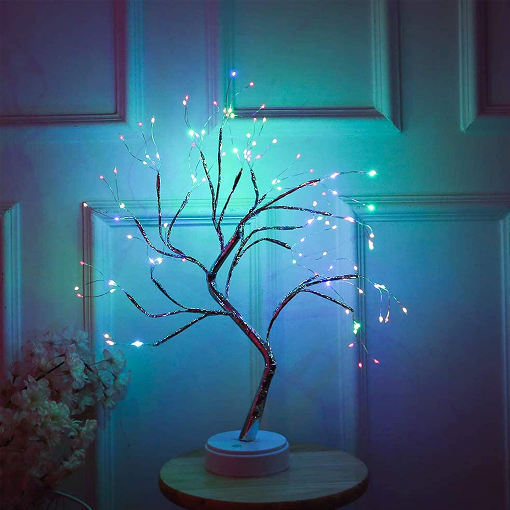 Ein dekorativer Baum mit LED-Lichtern. Er hat braune Äste mit bunten Lichtern auf einem Tisch. Der Hintergrund ist eine Wand.