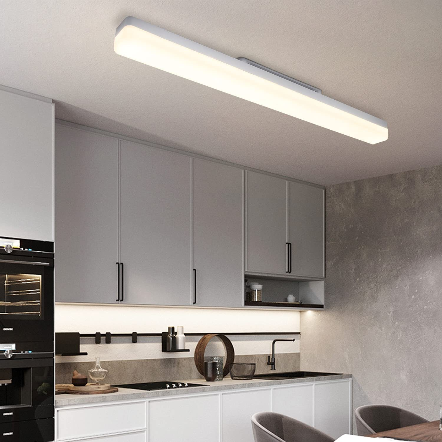 Una cucina moderna con una lunga lampada rettangolare sul soffitto. Sono visibili armadi grigi e un piano di lavoro scuro.