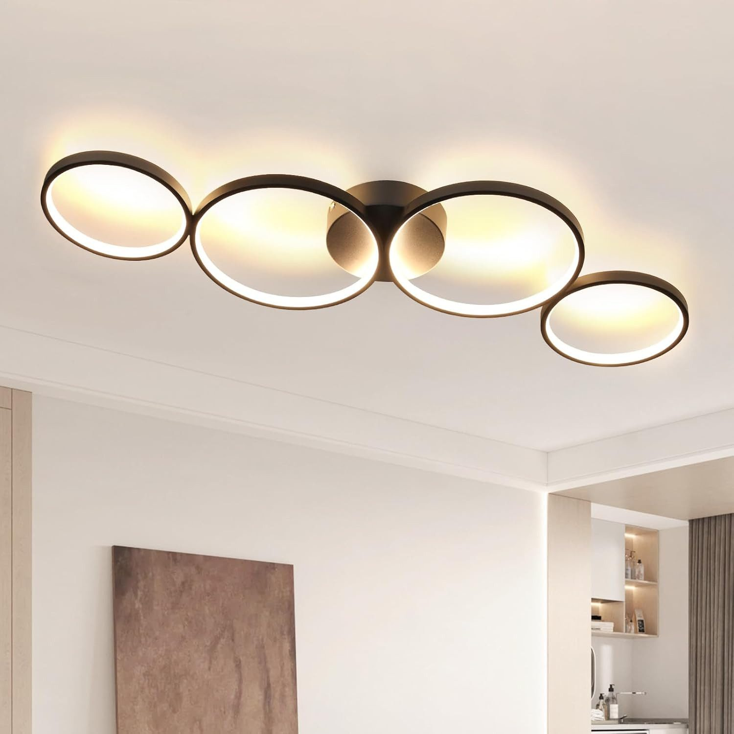 Una moderna plafoniera con quattro luci circolari interconnesse. La stanza ha pareti bianche e un dipinto marrone.