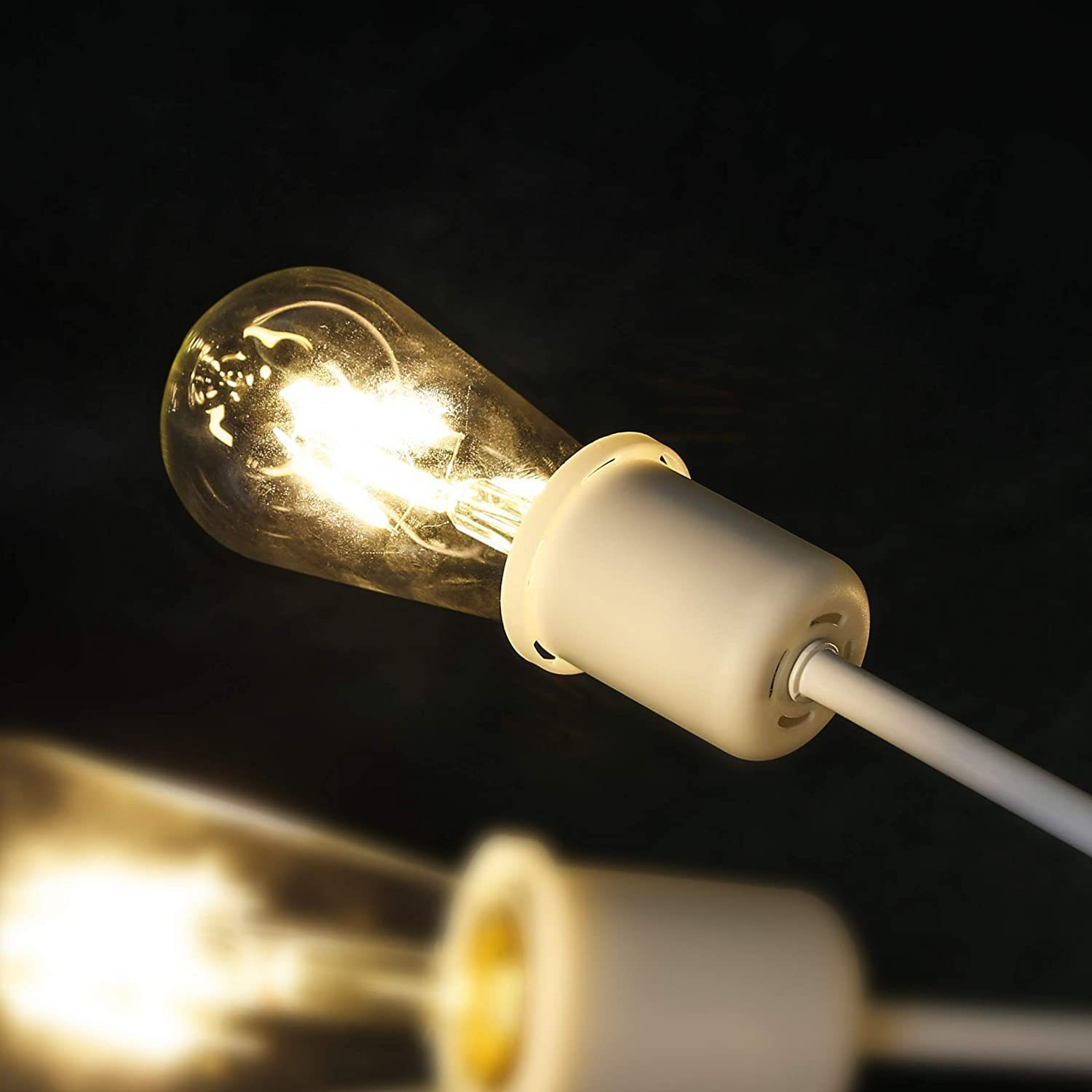 Zbliżenie zapalonej żarówki. Żarówka jest przezroczysta z żarnikiem, na ciemnym tle, z białą podstawą i przewodem.