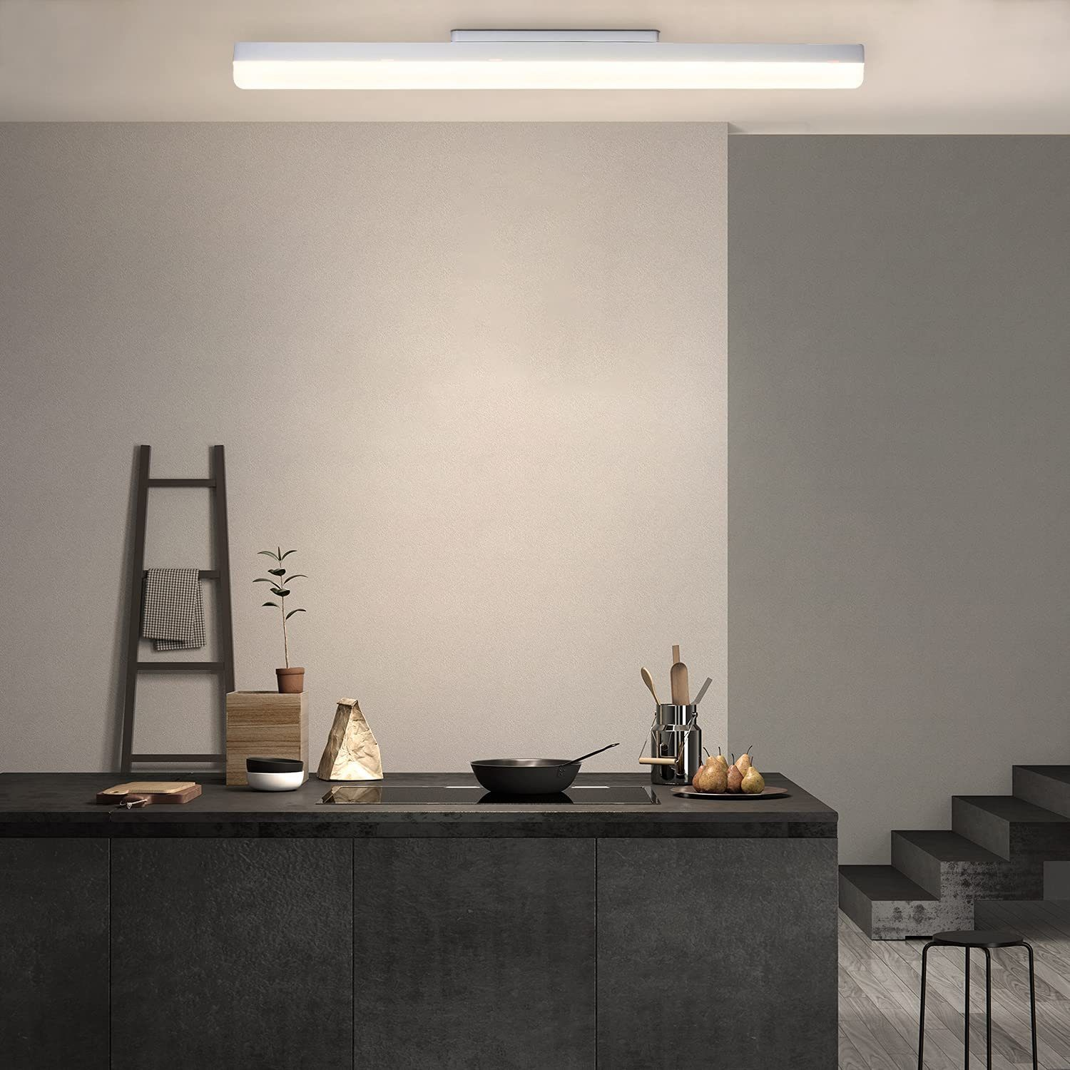Una cucina moderna con piano di lavoro nero e scala. Una pianta, pere e una padella sono sul bancone.