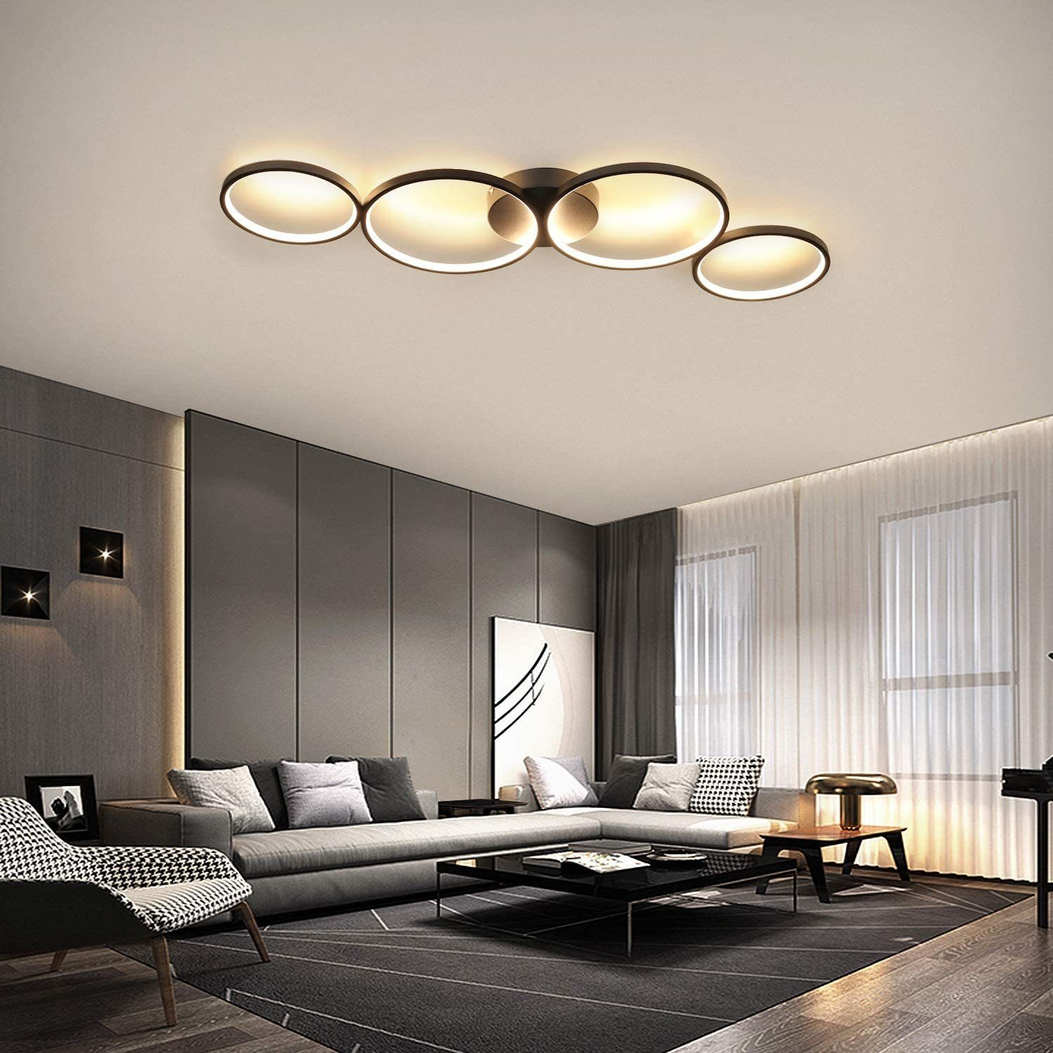 Soggiorno dal design moderno. Caratterizzato da un divano grigio, un tavolino nero, un lampadario e una sedia. Tende chiare.