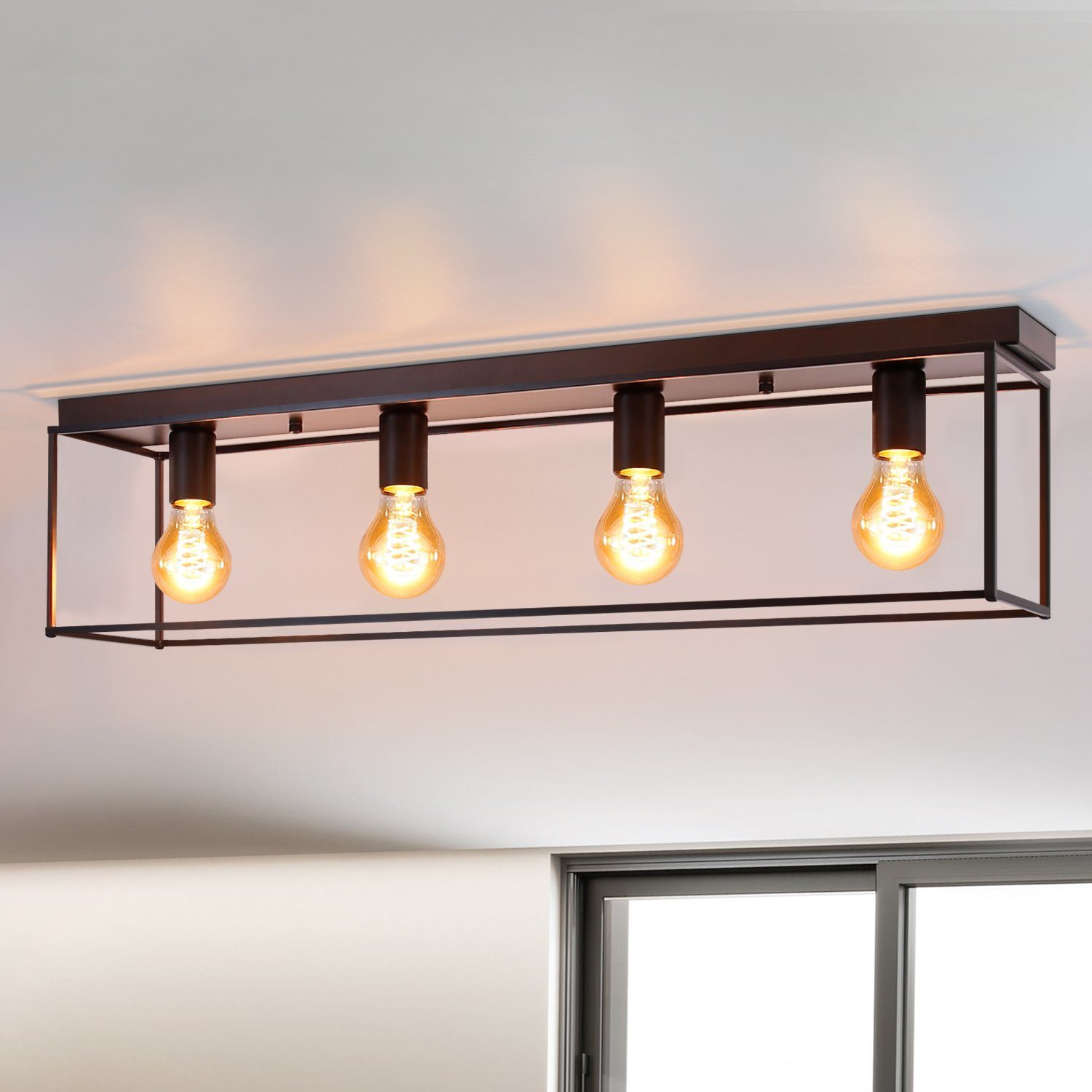 Un moderno lampadario a soffitto con quattro lampadine in stile Edison in una cornice rettangolare nera, contro un soffitto bianco.