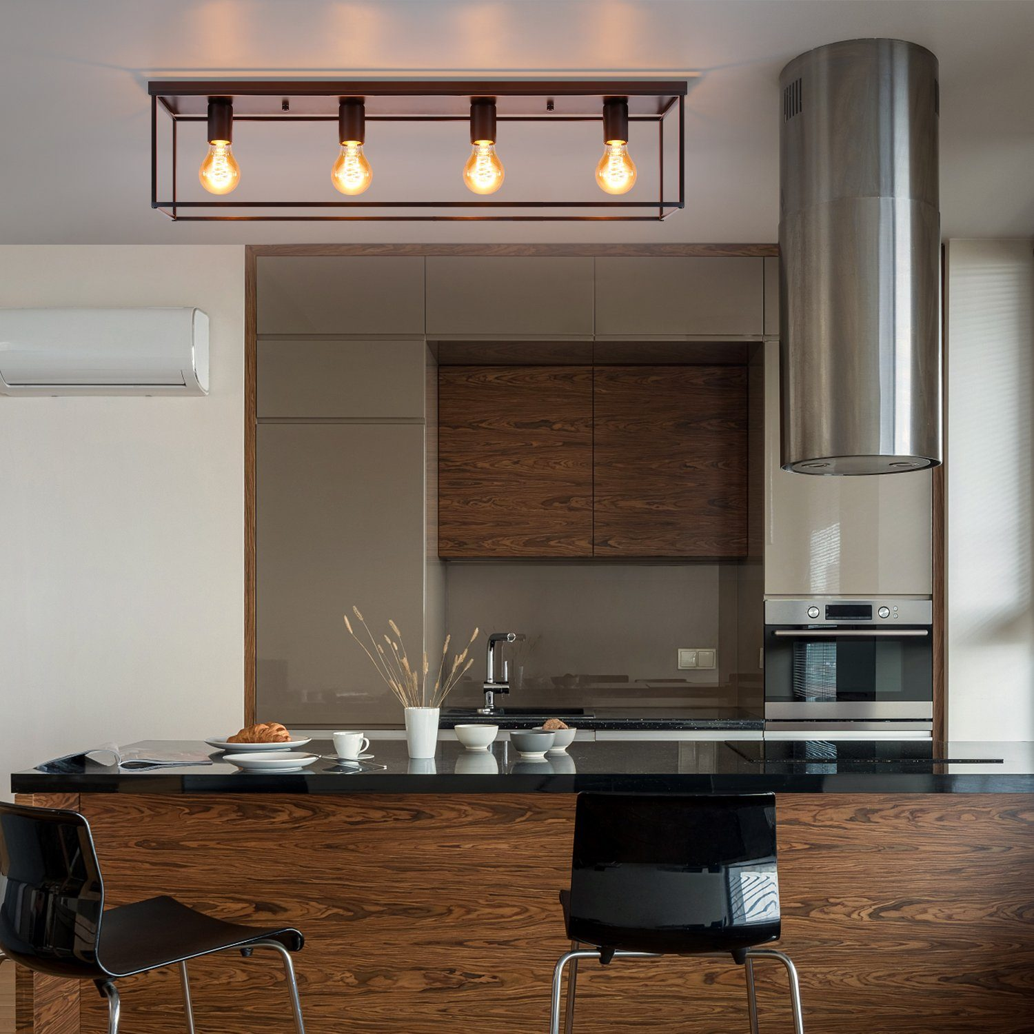 Cucina moderna con piano di lavoro nero, mobili in legno e cappa in metallo. Lampade sospese. Due sedie nere al bancone.