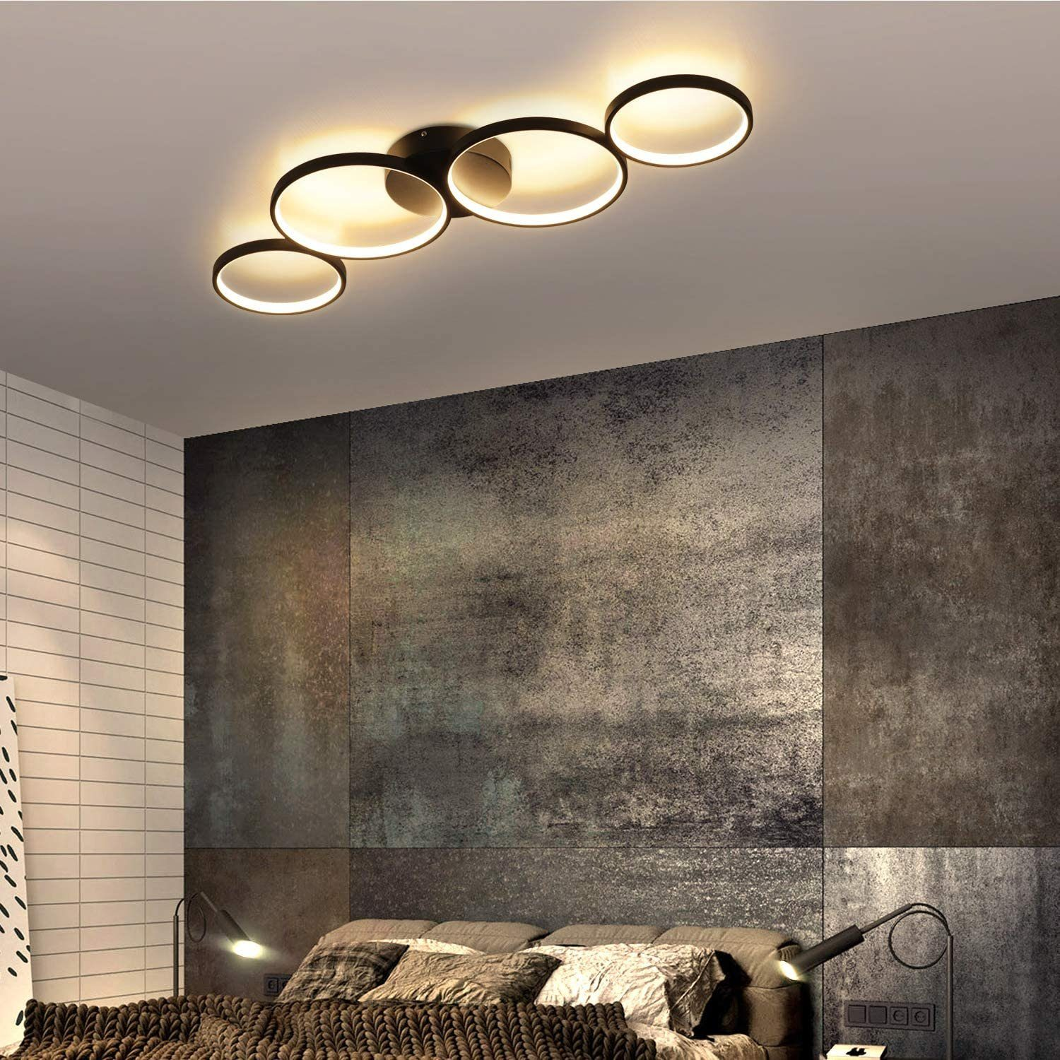 Camera da letto con lampada da soffitto moderna, letto e parete strutturata. La luce è circolare, il letto ha cuscini e una coperta.