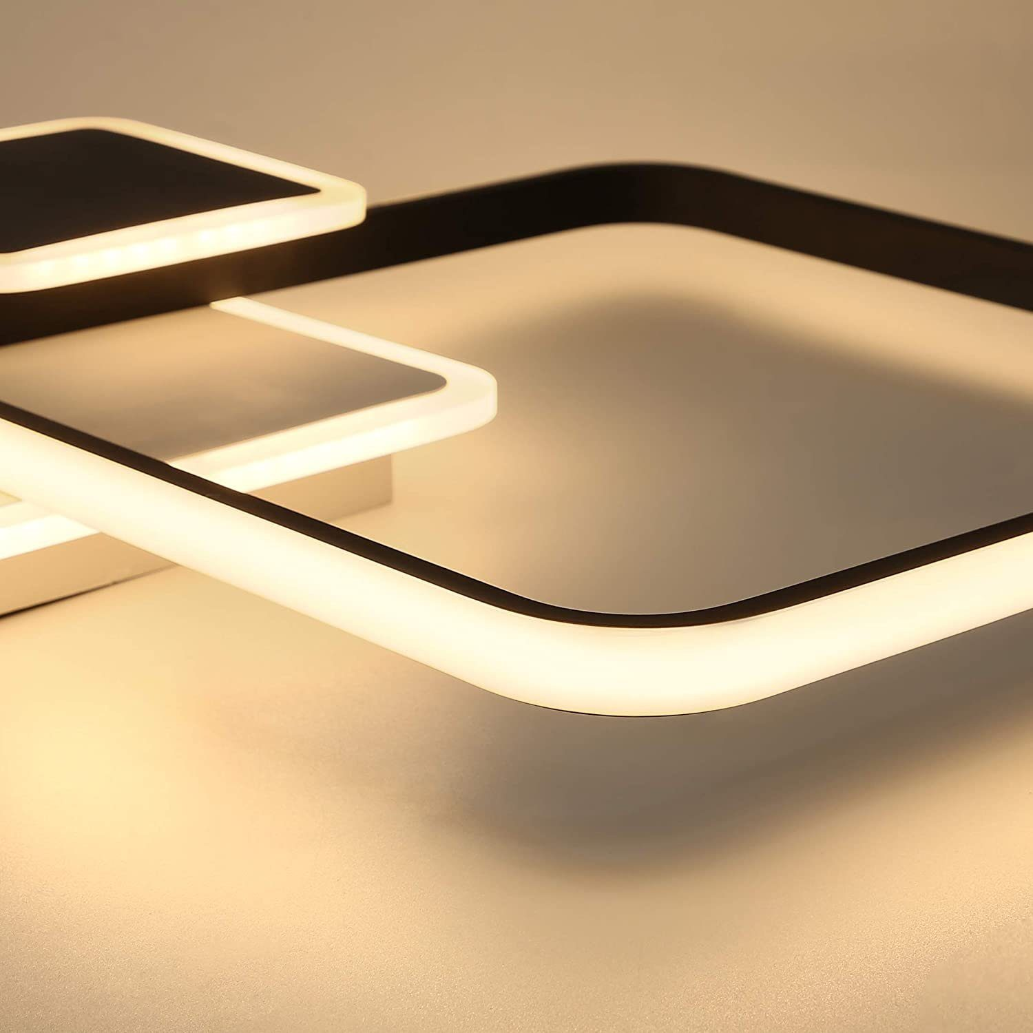 Nahaufnahme einer modernen Deckenleuchte. Sie hat schwarze Rahmen mit weißen LED-Leuchten in einem geometrischen Design vor beigem Hintergrund.