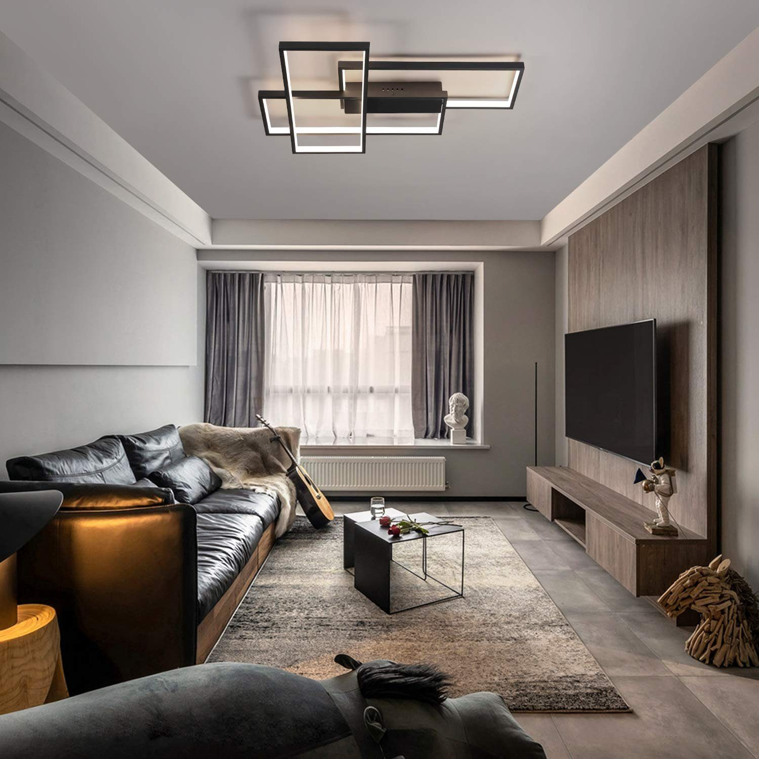 Salón con sofá de cuero, TV, alfombra, guitarra e iluminación moderna. Ventana con cortinas y mesa de centro decorada.