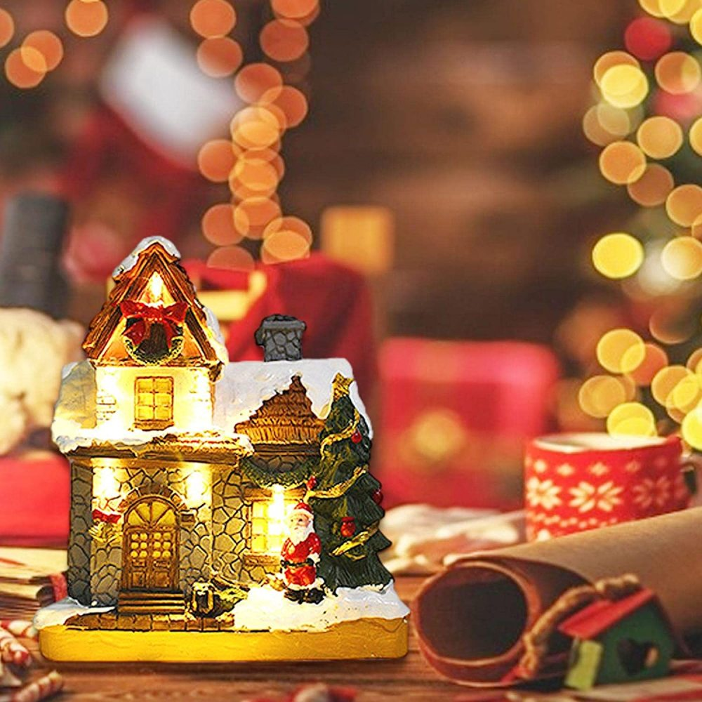 Ein beleuchtetes Weihnachtshaus mit einer Santa-Figur und einem Weihnachtsbaum. Der Hintergrund hat Bokeh-Lichter, eine Tasse und ein gerolltes Papier.