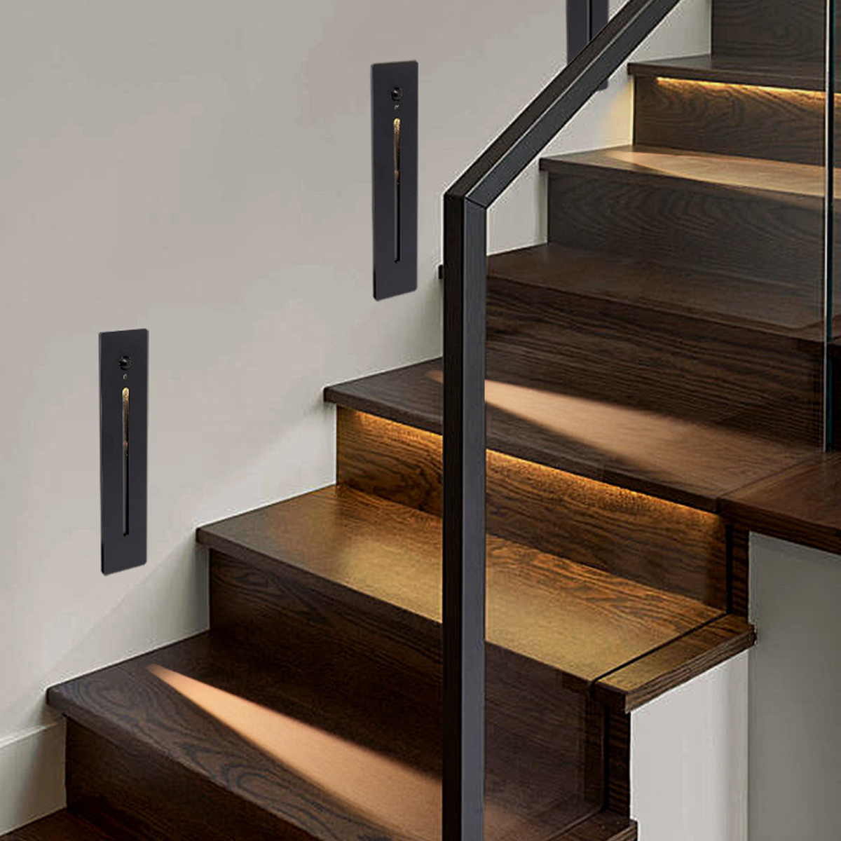 Holztreppe mit schwarzem Metallgeländer. Lichter an der Wand und unter der Treppe. Die Wand ist beige.
