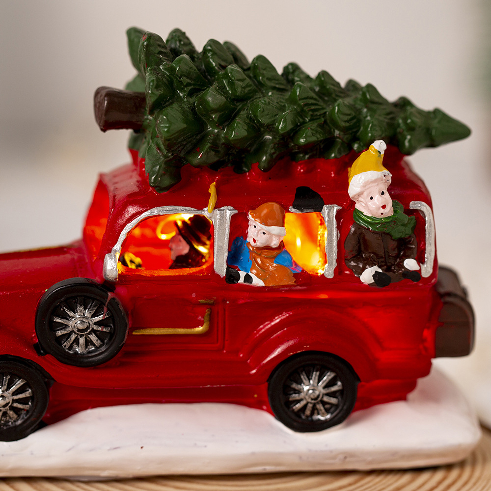 Ein rotes Spielzeugauto mit Figuren im Inneren und einem Weihnachtsbaum oben drauf. Das Auto steht auf weißer Basis.