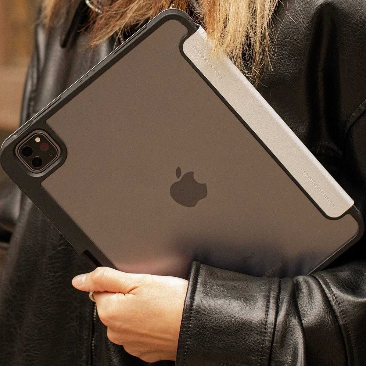 Una persona tiene in mano un iPad grigio in una custodia nera. Il logo Apple è visibile. La persona indossa una giacca di pelle nera.