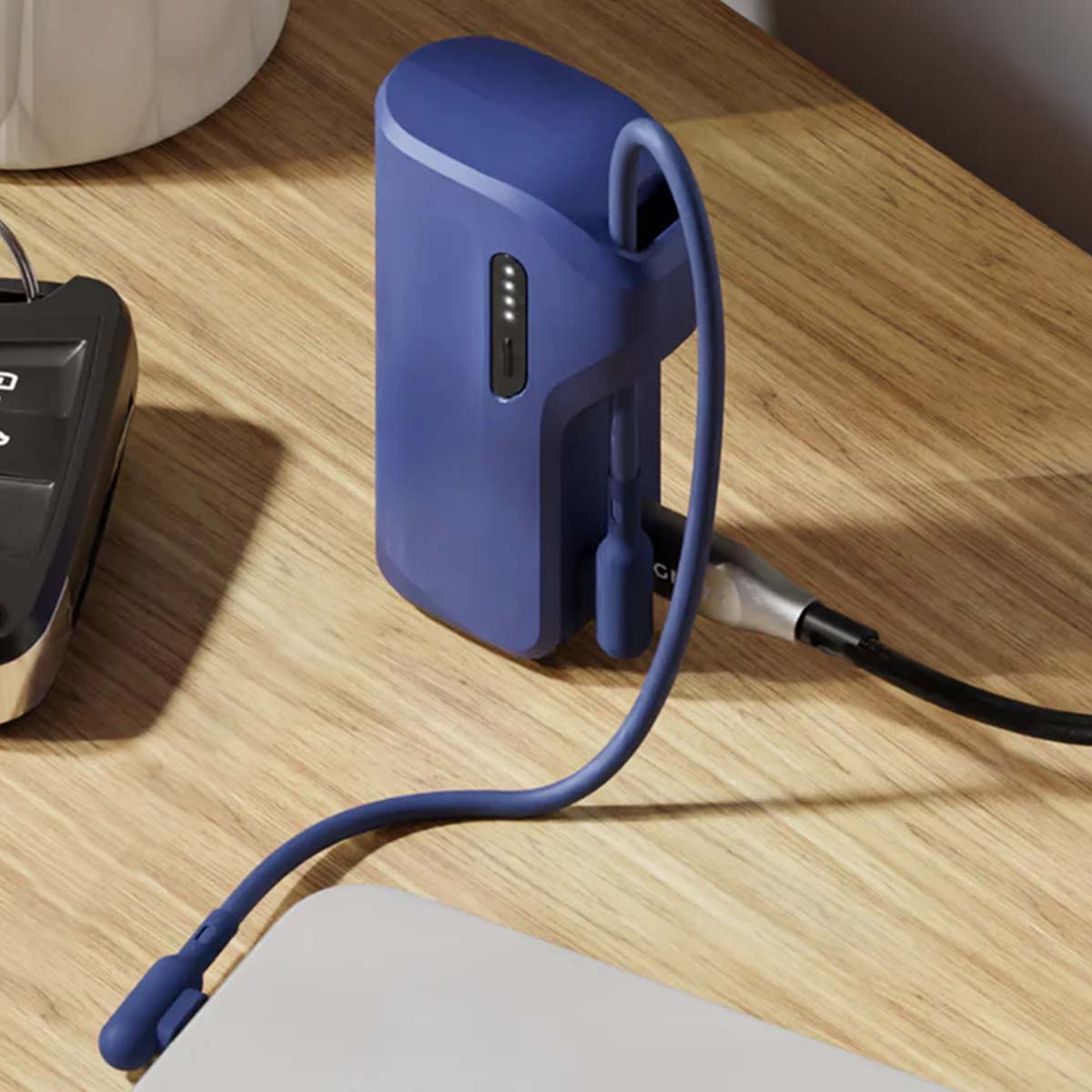 Un power bank blu con un cavo collegato su un tavolo di legno. Un chiave di macchina e un oggetto bianco sono anch'essi sul tavolo.