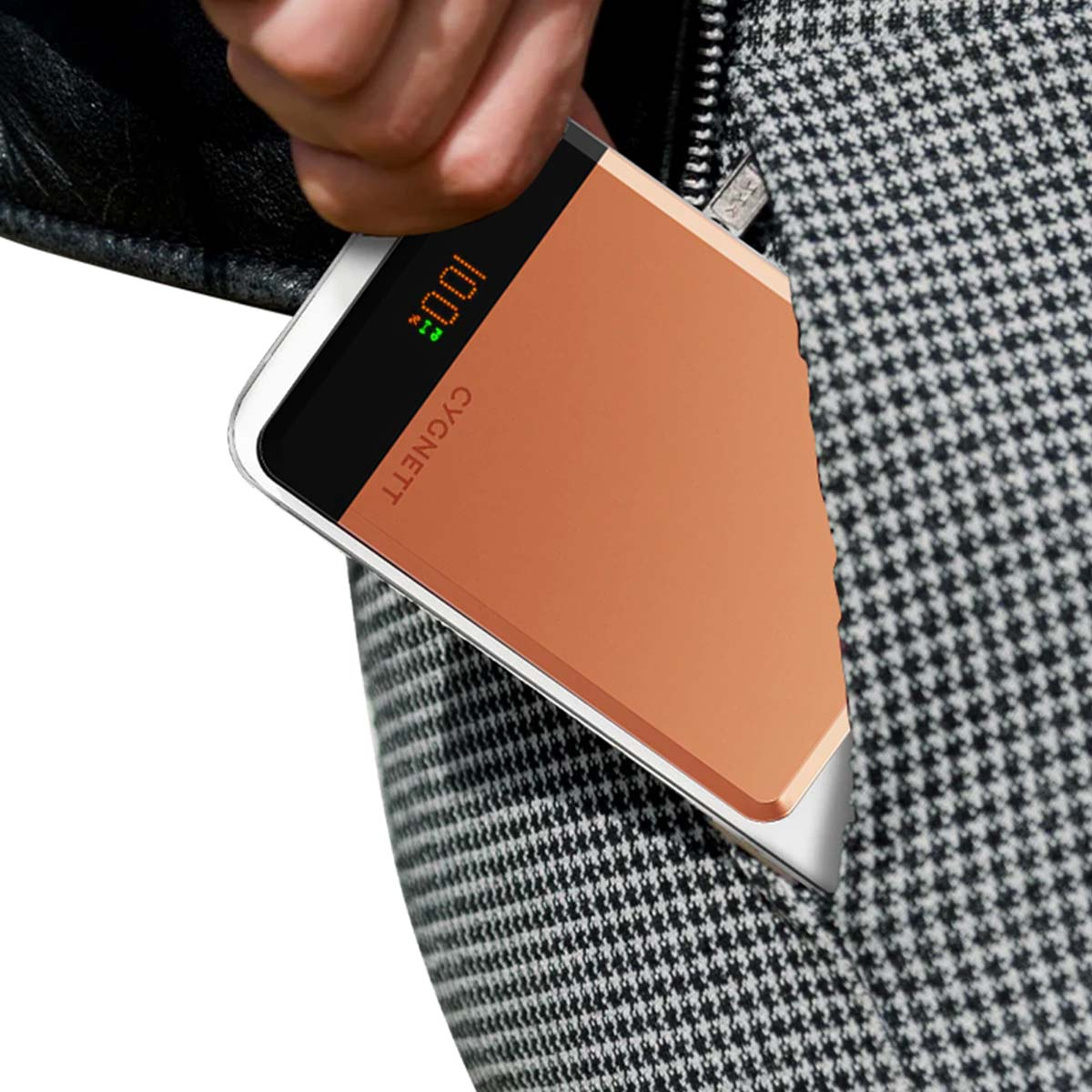 Una mano tiene un power bank CYGNETT. Il power bank è color rame e mostra 100%. La persona indossa una giacca a pied de poule.