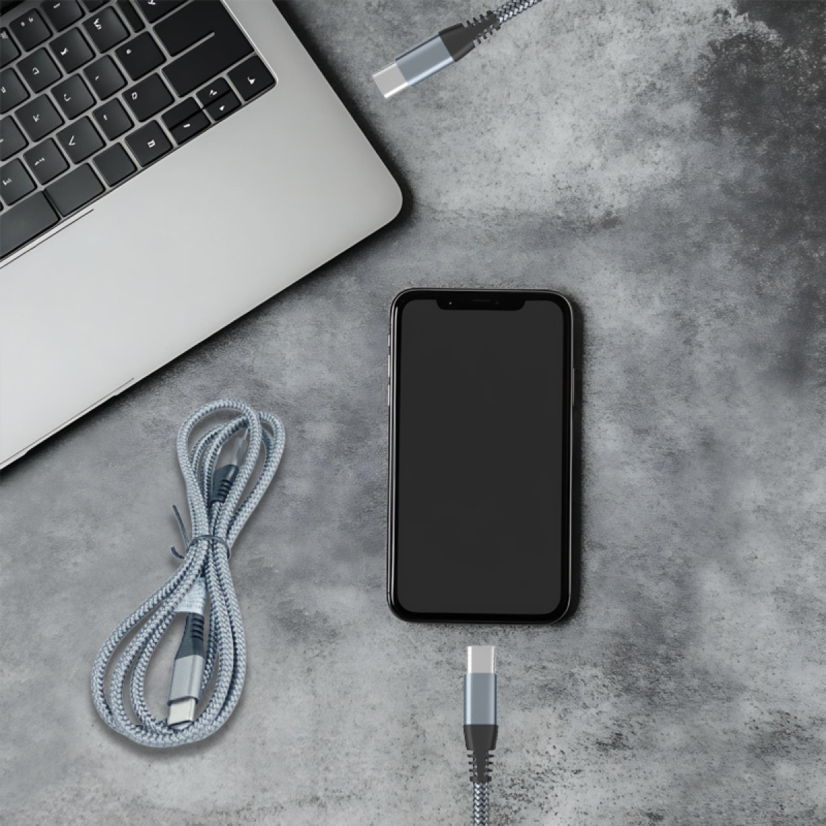 Auf einer grauen Oberfläche liegen ein Laptop, ein Smartphone und Ladekabel. Das Telefon ist zentriert, Kabel liegen herum. Der Laptop ist links oben.