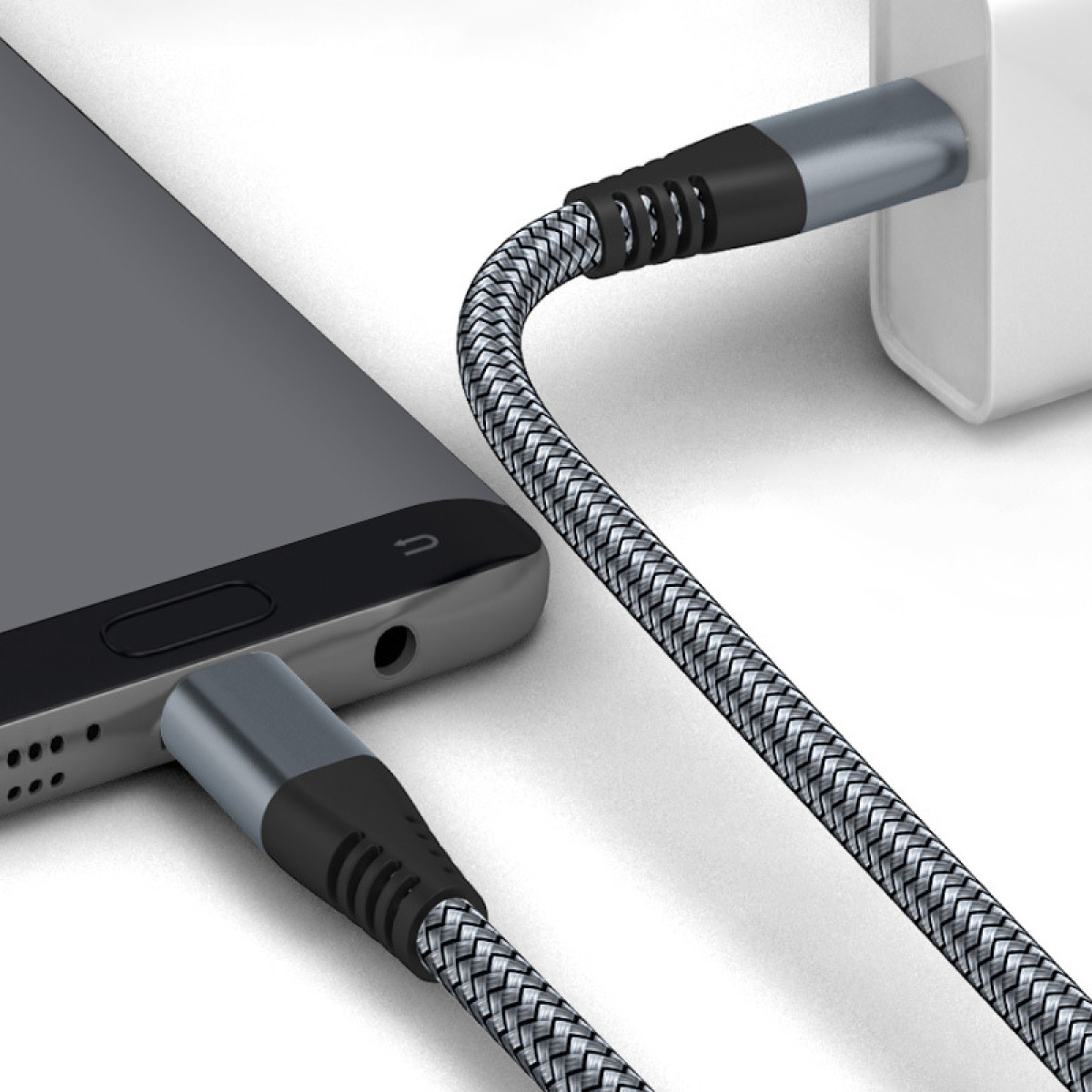 Uno smartphone è in carica con un cavo intrecciato. Il telefono è grigio e il caricabatterie bianco. Il cavo ha dettagli neri e grigi.