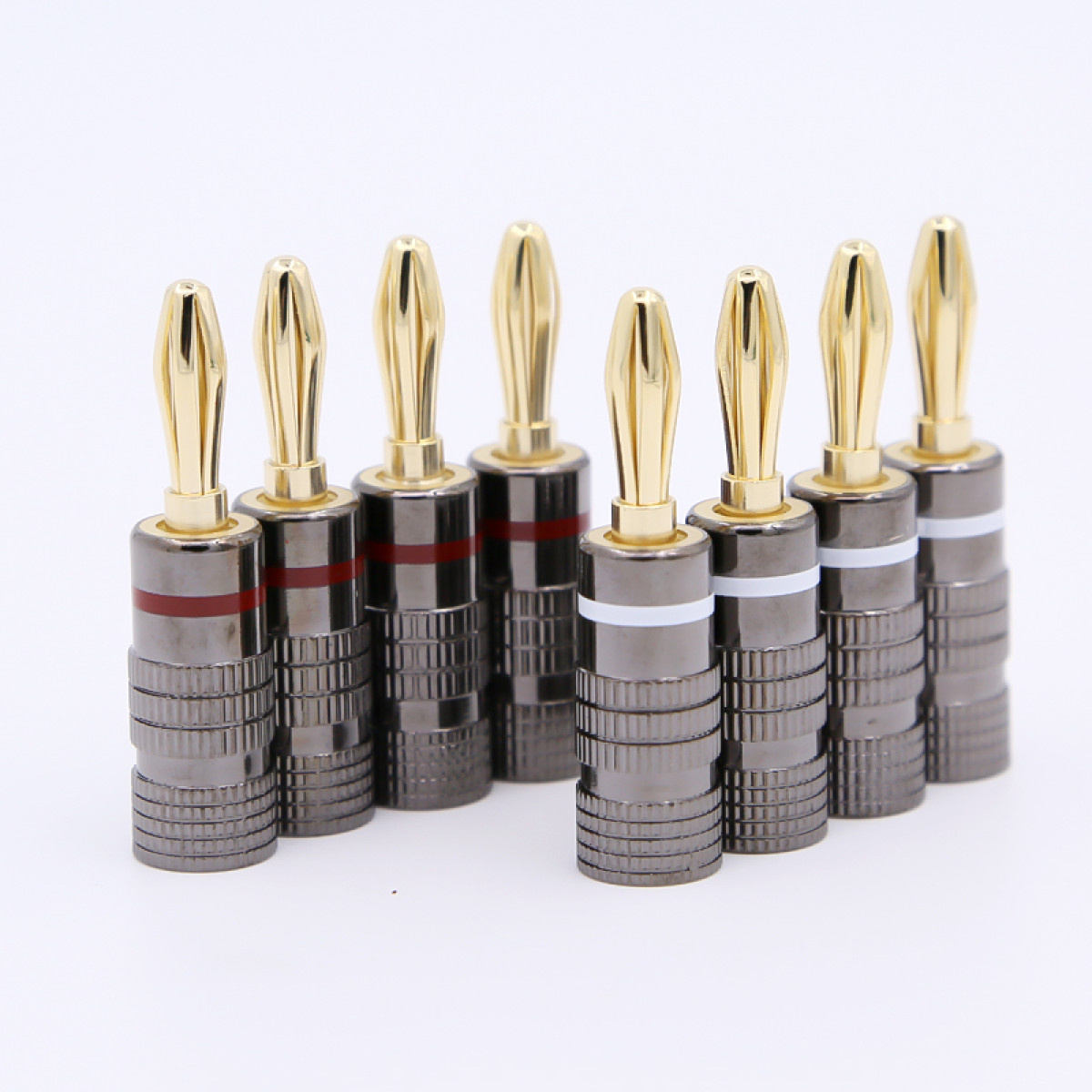 Neun goldspitzen Bananenstecker auf weißem Hintergrund. Stecker haben einen metallgrauen Körper mit roten und weißen Bändern.
