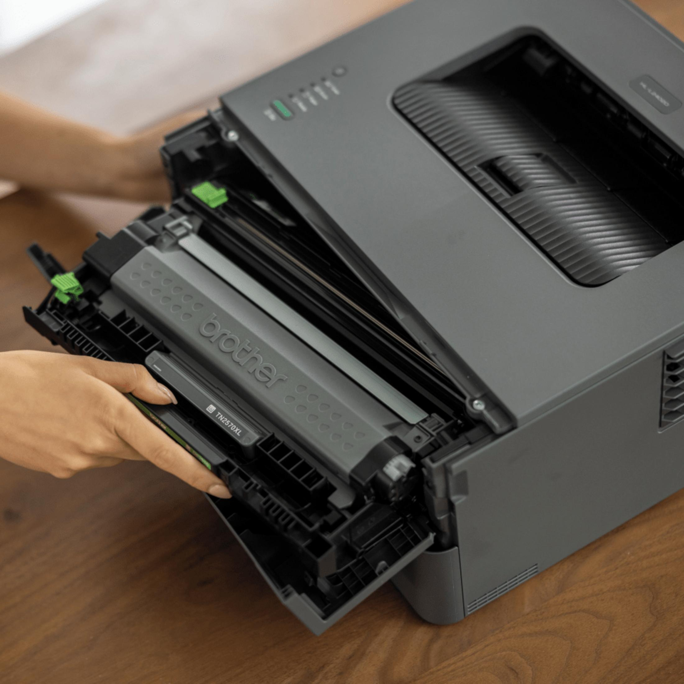 Una persona sta installando una cartuccia toner Brother in una stampante laser grigia. La stampante è su un tavolo di legno.