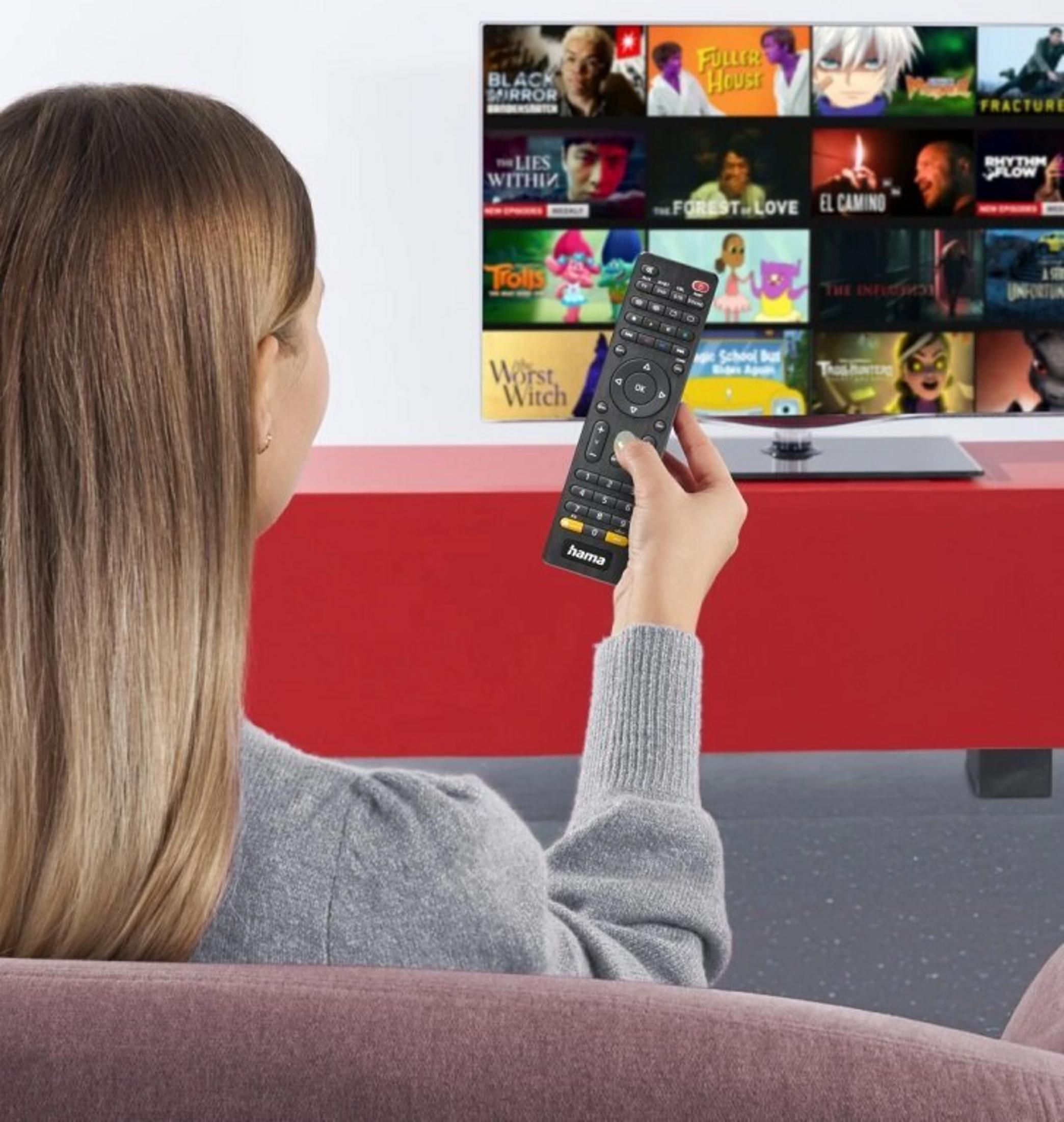 Kobieta trzyma pilota przed telewizorem. Na ekranie widać różne filmy i programy telewizyjne.