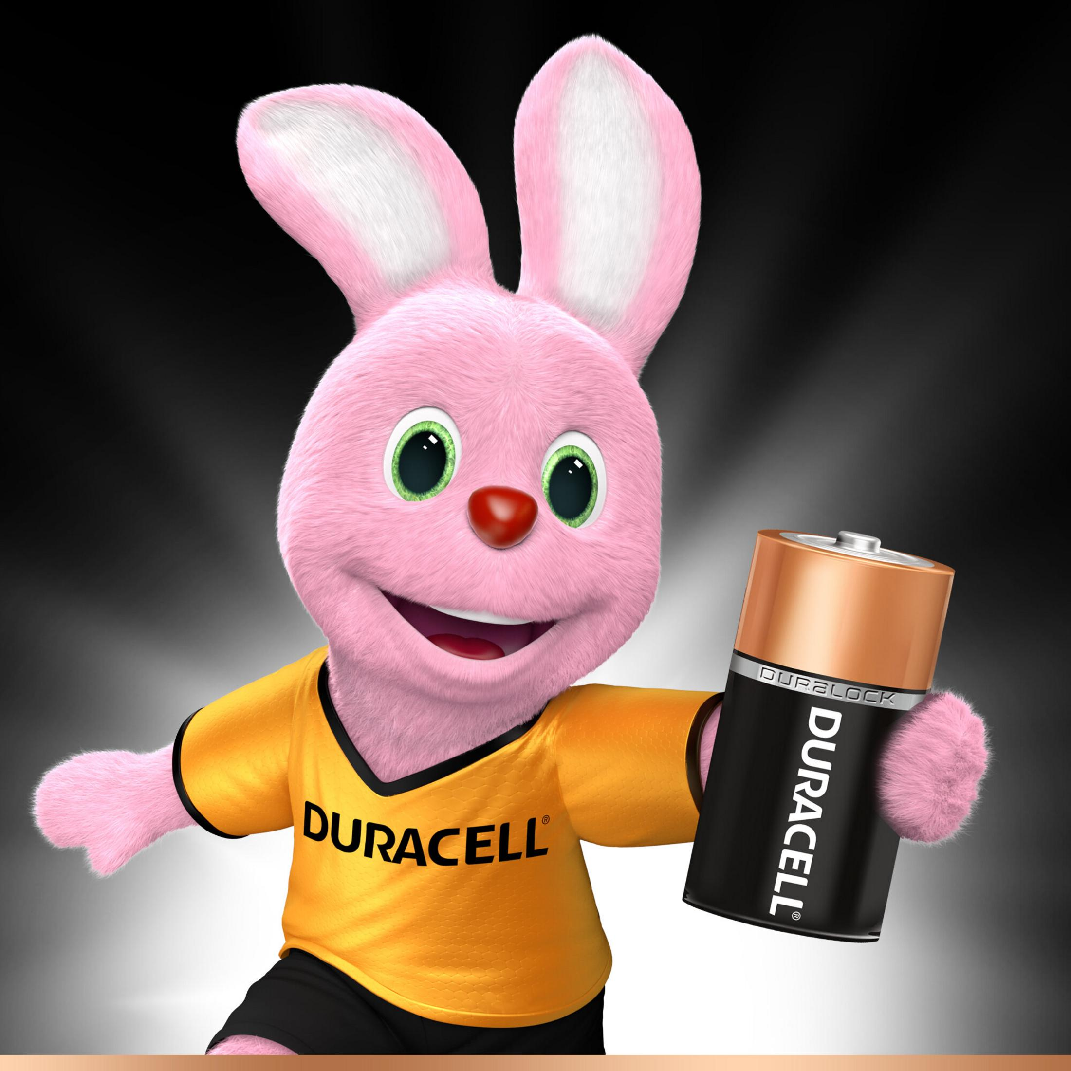 Różowy królik Duracell trzymający baterię Duracell, w żółtej koszulce i czarnych szortach, na czarnym tle.