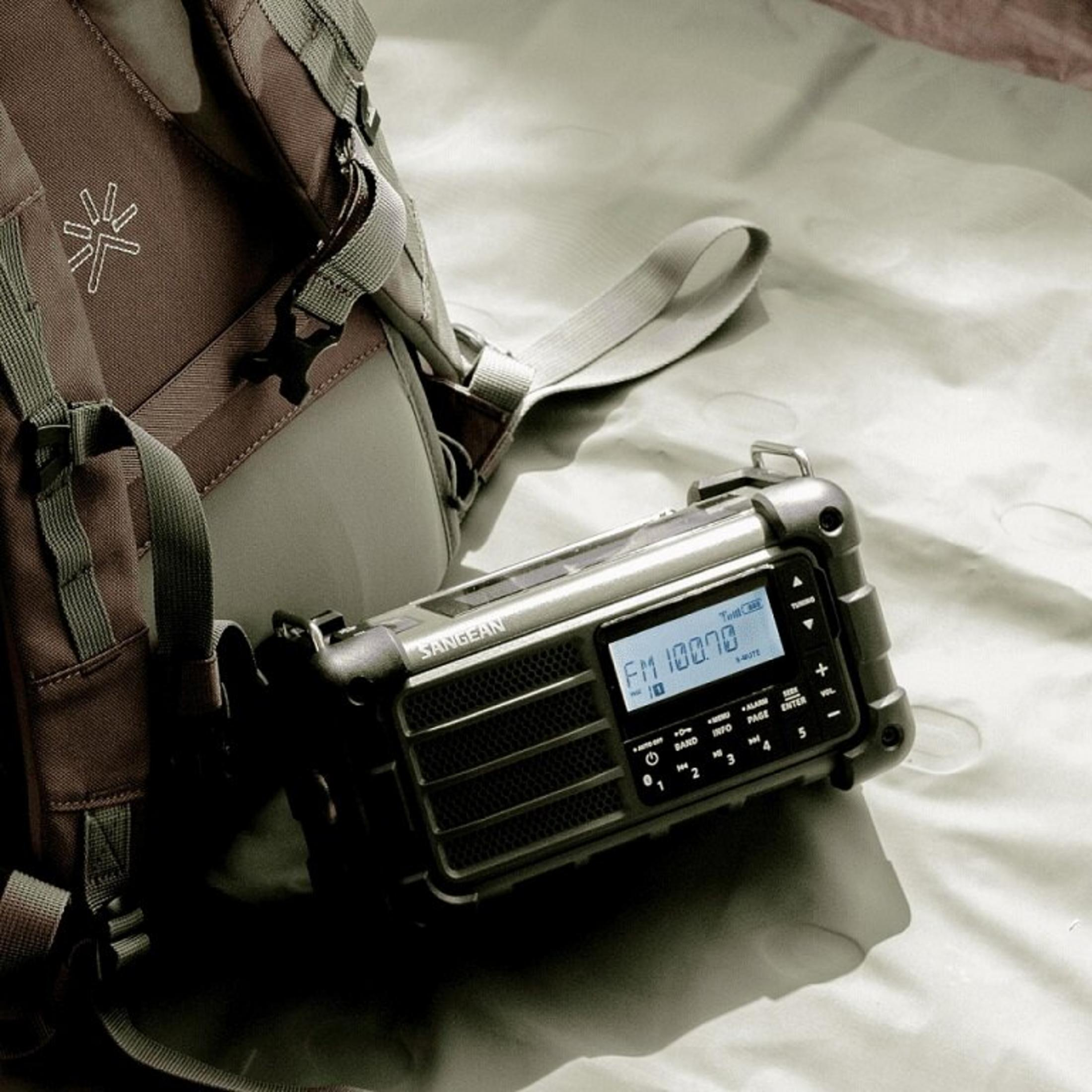 Una radio con display digitale e uno zaino su una superficie chiara.