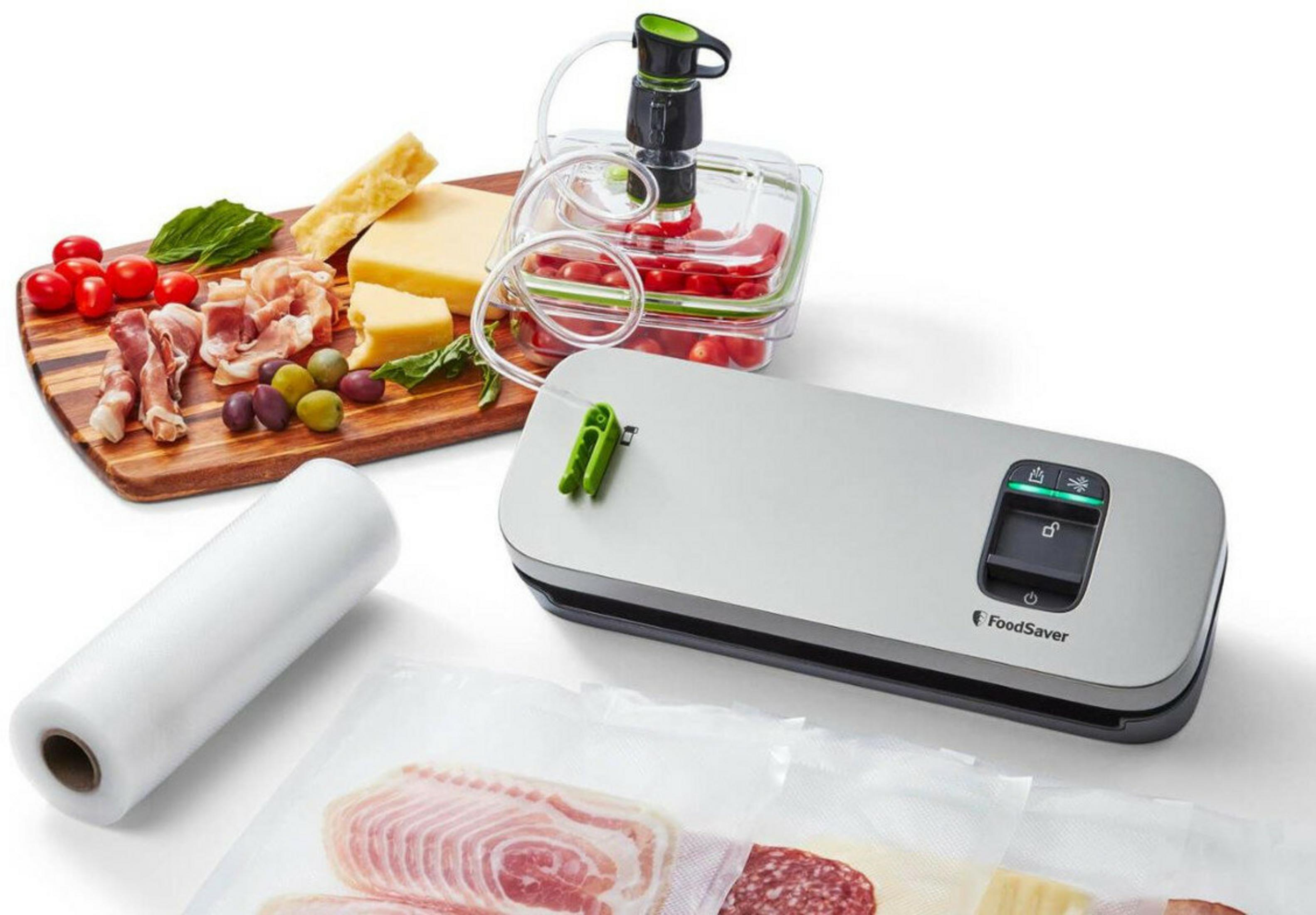 Ein Foodsaver-Gerät mit Lebensmitteln wie Tomaten, Käse, Fleisch und Oliven auf einem Holzbrett.