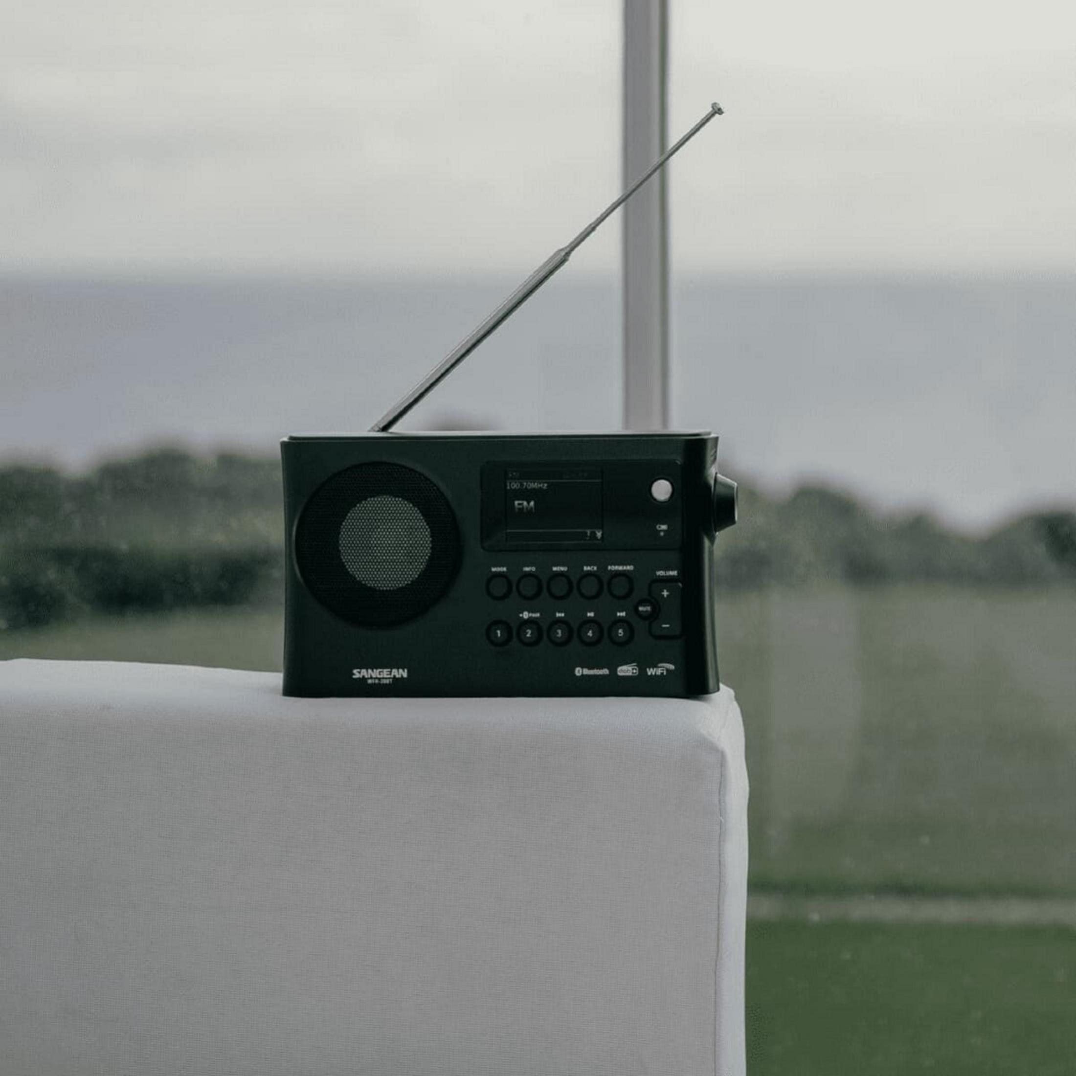 Une radio noire avec une antenne est posée sur une surface blanche, avec vue sur la mer à travers une fenêtre.