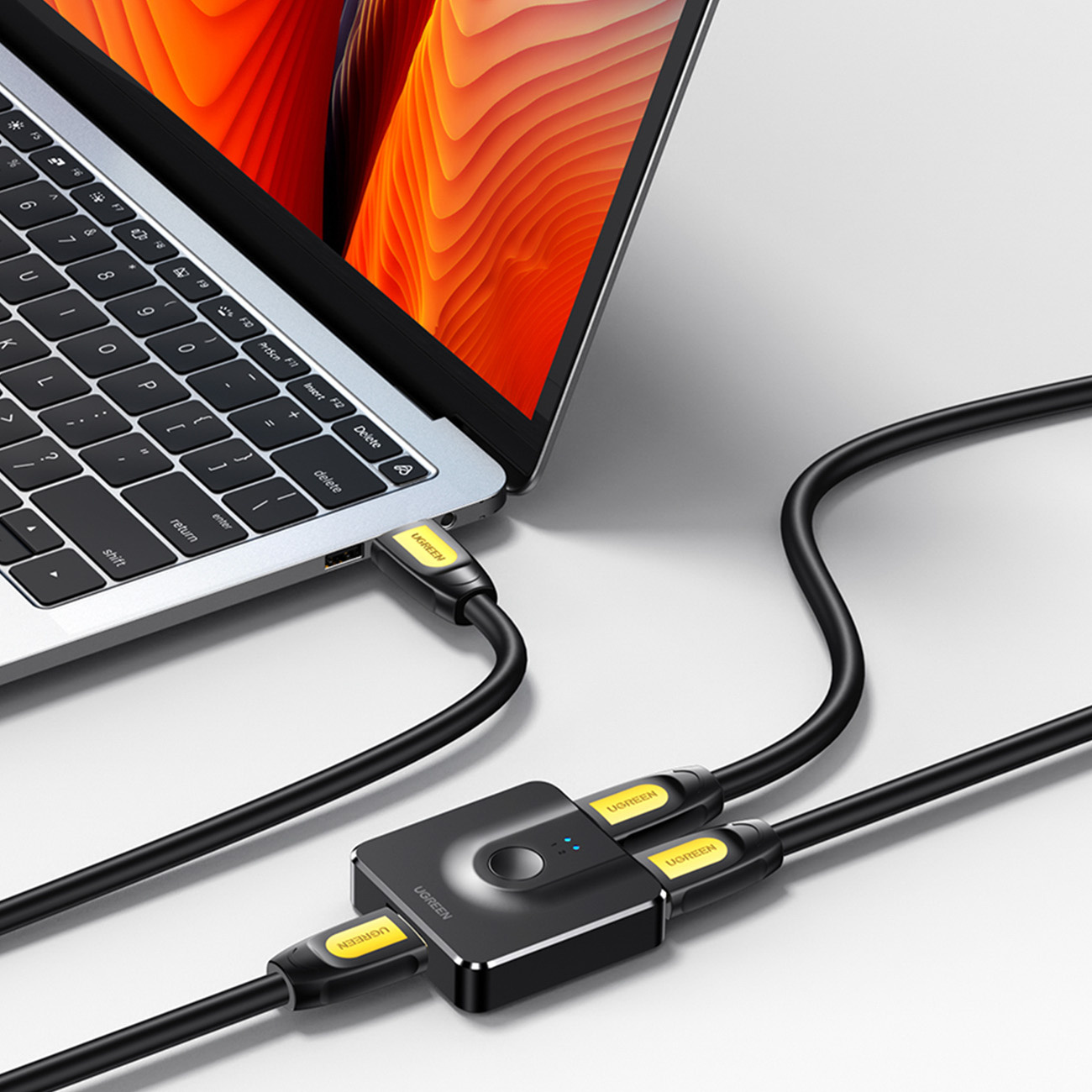 Laptop podłączony do czarnego urządzenia UGREEN za pomocą czarnego kabla. Ekran laptopa wyświetla pomarańczowy i żółty.