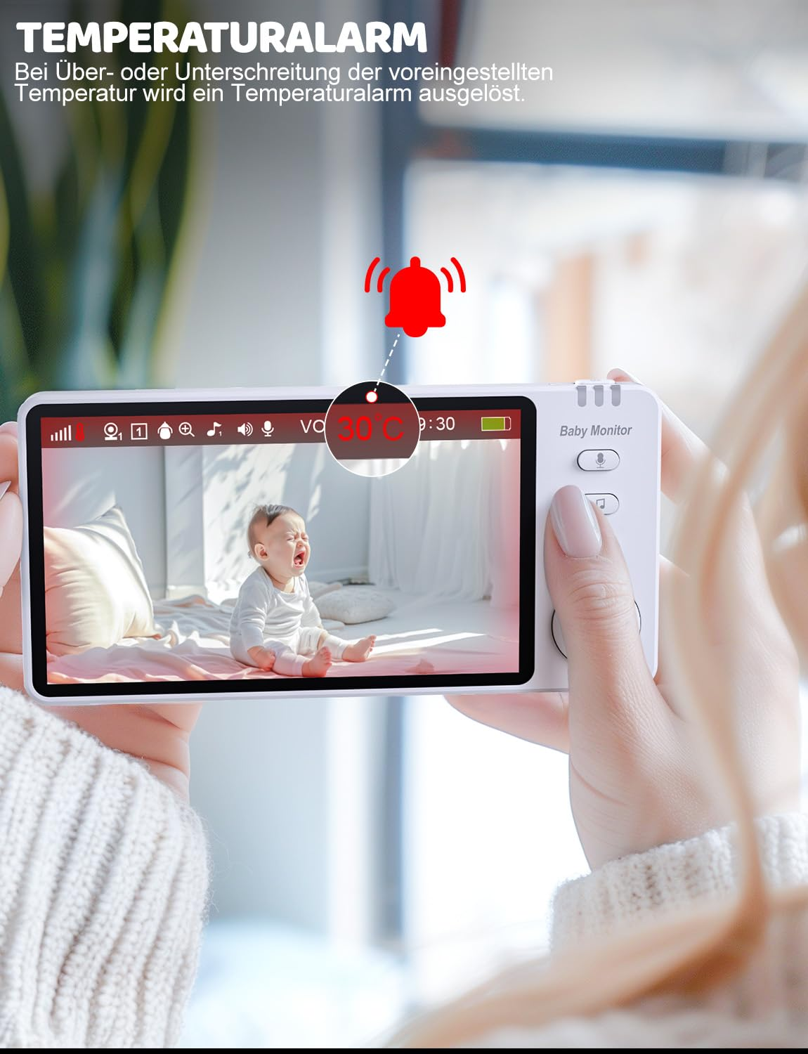 Ein Babyphone zeigt ein weinendes Baby. Der Monitor zeigt 30 Grad Celsius. Ein Alarmsymbol ist sichtbar. Das Gerät wird von einer Person gehalten.
