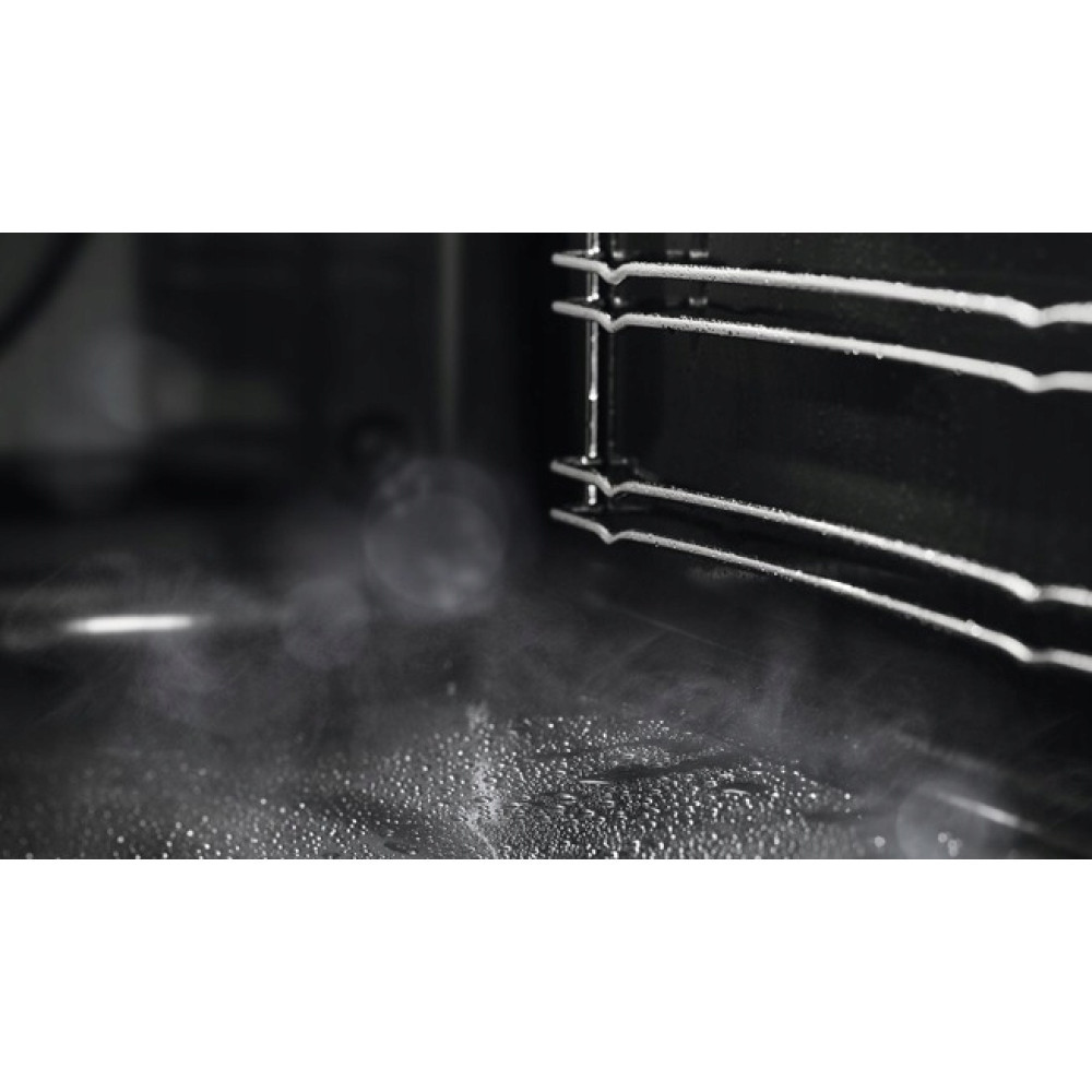 Wnętrze piekarnika. Skraplanie wody i para na dnie. Metalowy ruszt w prawym górnym rogu. Ciemne otoczenie.