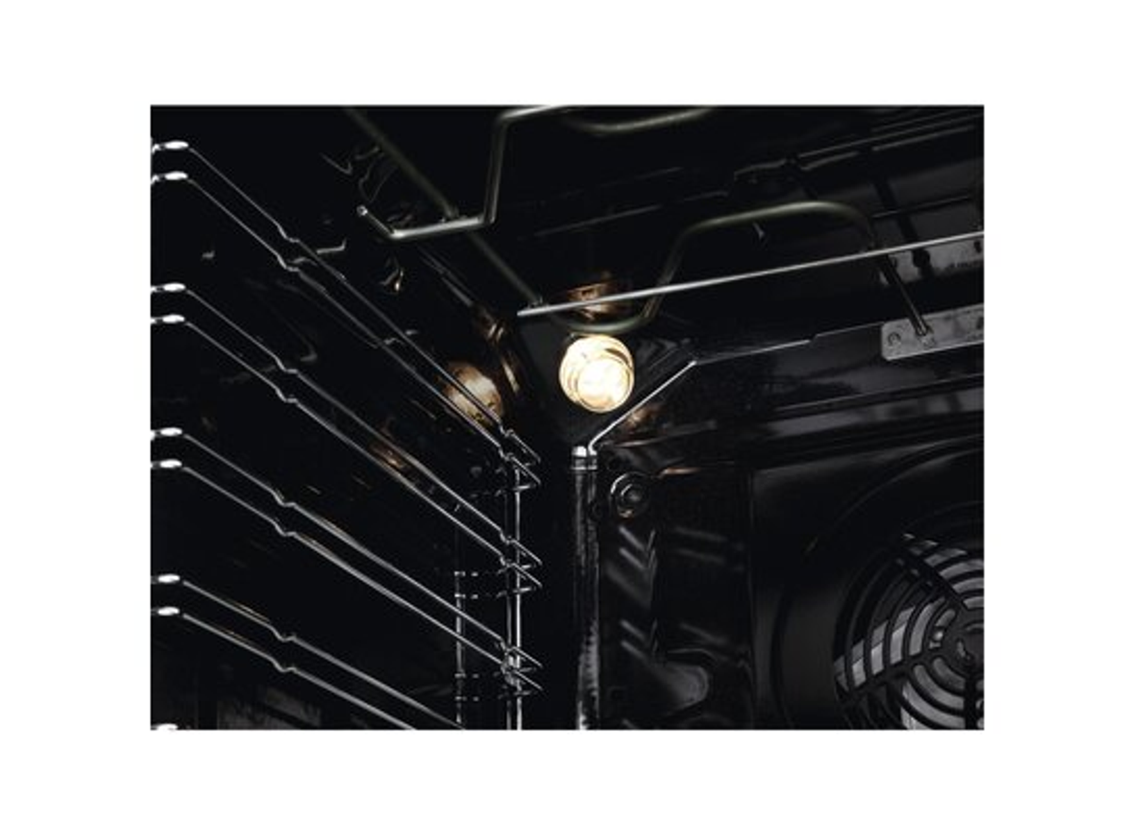 Wnętrze piekarnika z rusztami, jasną żarówką i wentylatorem. Wnętrze jest ciemne z metalowymi elementami i świecącym światłem.