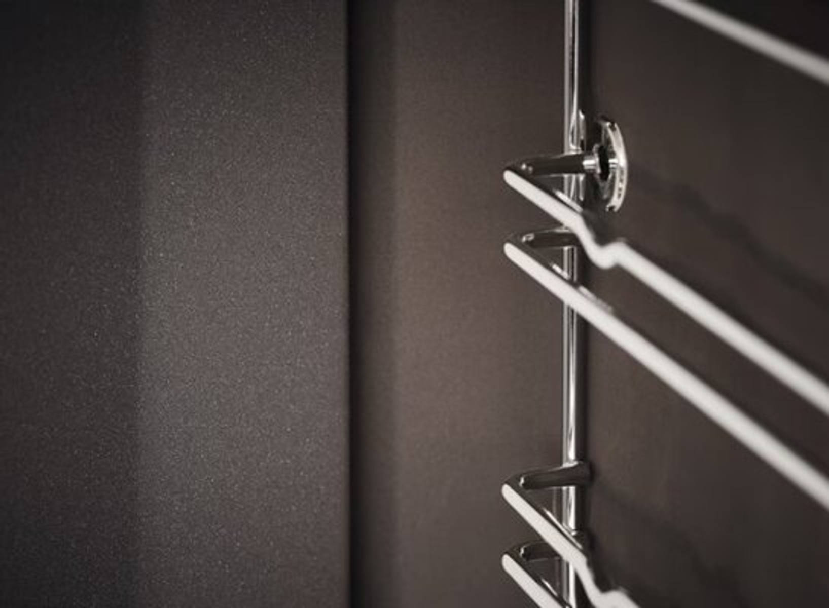 Zbliżenie chromowanego wieszaka na ręczniki zamontowanego na ciemnobrązowej ścianie. Wieszak ma minimalistyczny design z trzema poziomymi prętami.