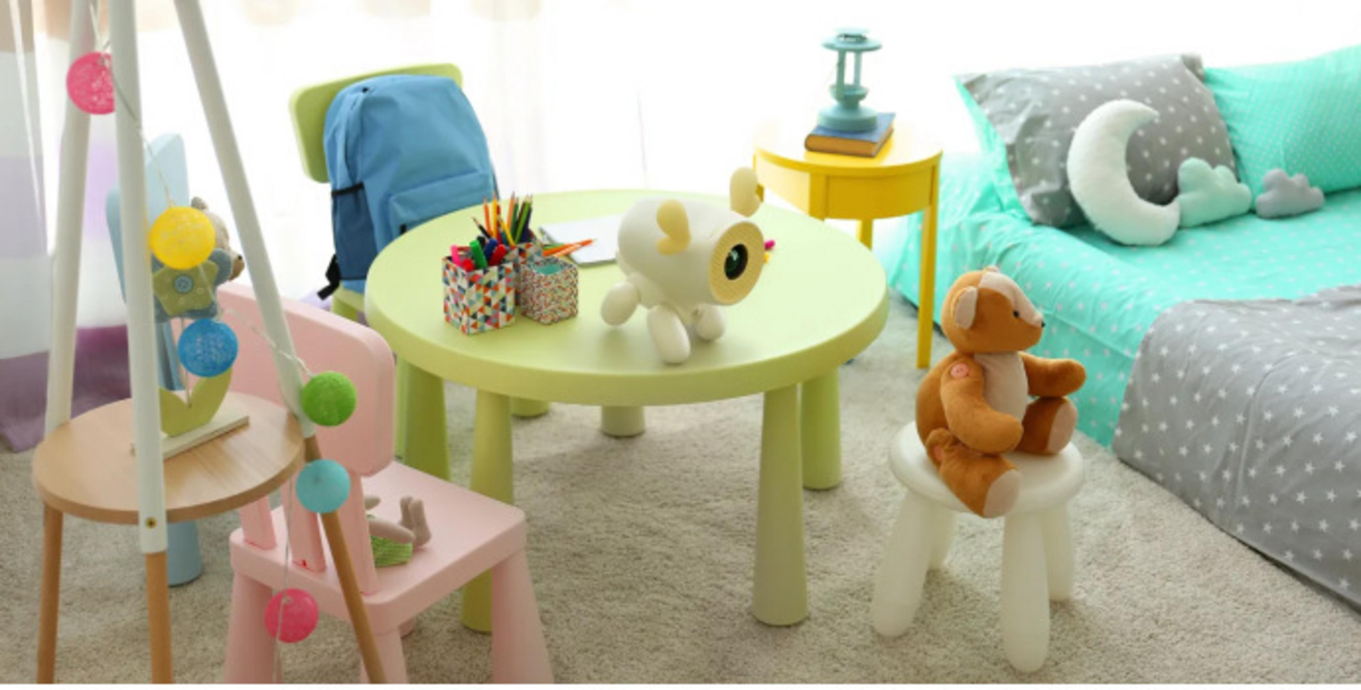 Ein Kinderzimmer mit Tisch, Stühlen, Spielzeug und einem Bett. Das Zimmer ist mit Pastellfarben und weichen Möbeln dekoriert.