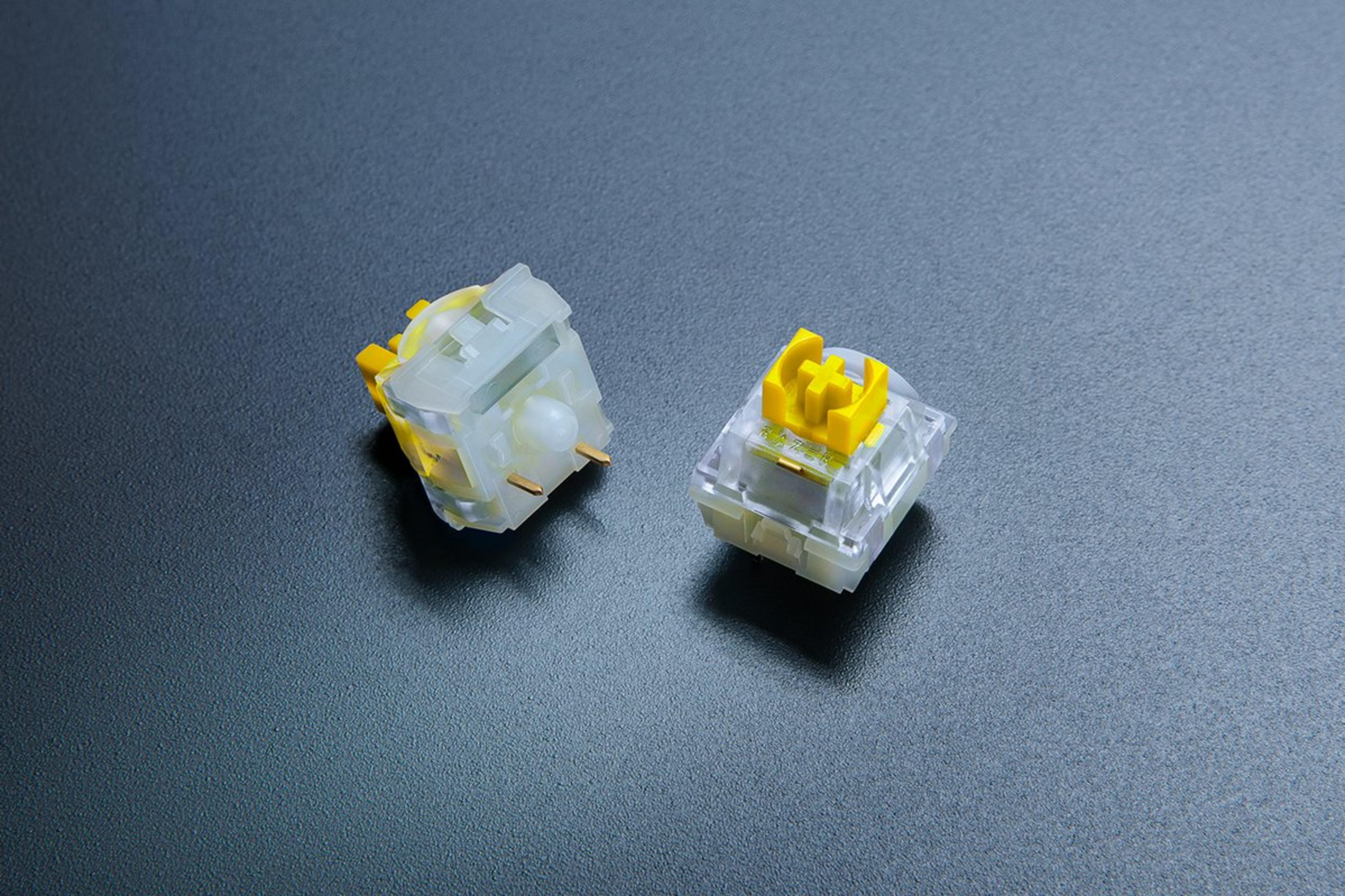 Zwei mechanische Tastaturschalter. Einer ist transparent mit gelben Akzenten, der andere ist gelb. Beide liegen auf dunkler Oberfläche.