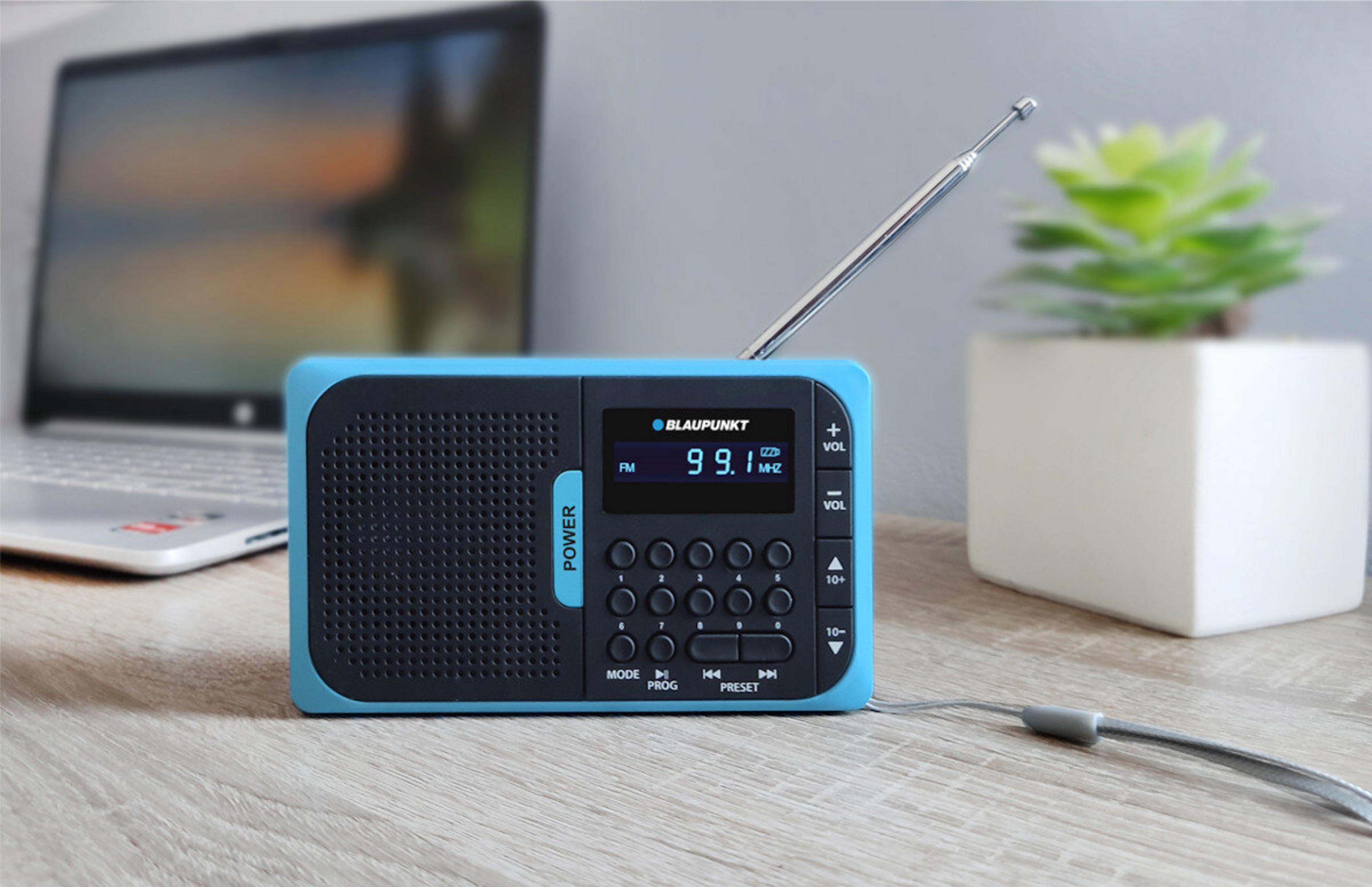 Una radio Blaupunkt blu e nera con antenna argentata, accanto a un laptop e una piccola pianta in vaso bianco.