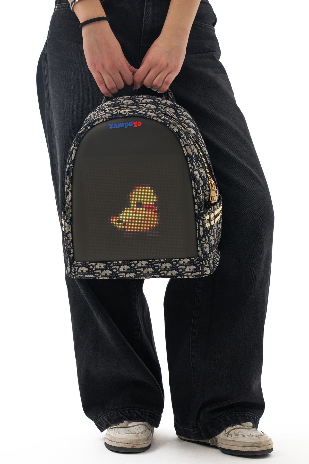 Bir kişi üzerinde pikselli bir ördek bulunan bir sırt çantası tutuyor. Çantanın üstünde bir logo var. Kişi siyah kot pantolon ve beyaz ayakkabı giyiyor.