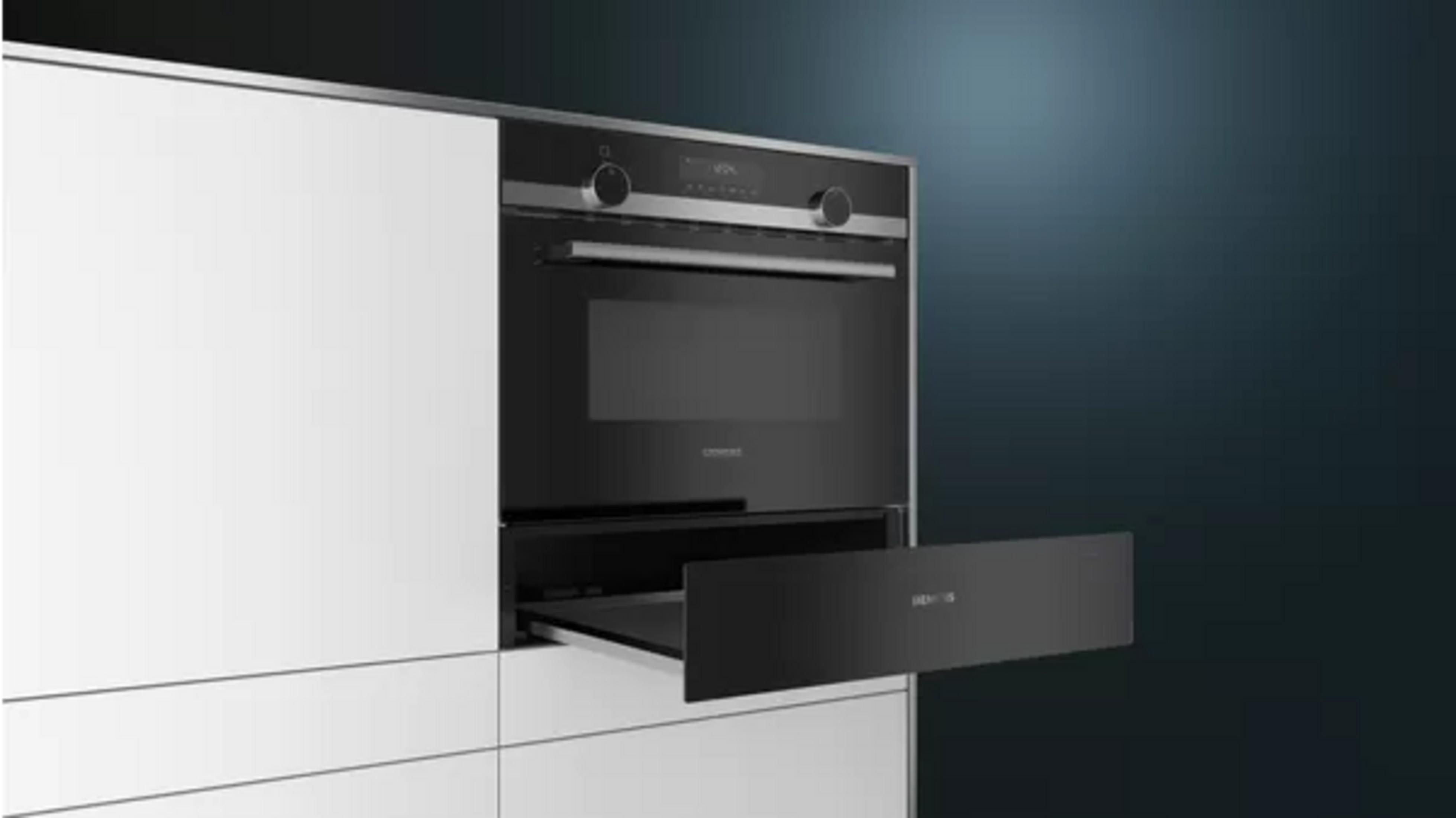 Un moderno forno nero è integrato in armadi bianchi. Il cassetto del forno è aperto. Lo sfondo è blu scuro.