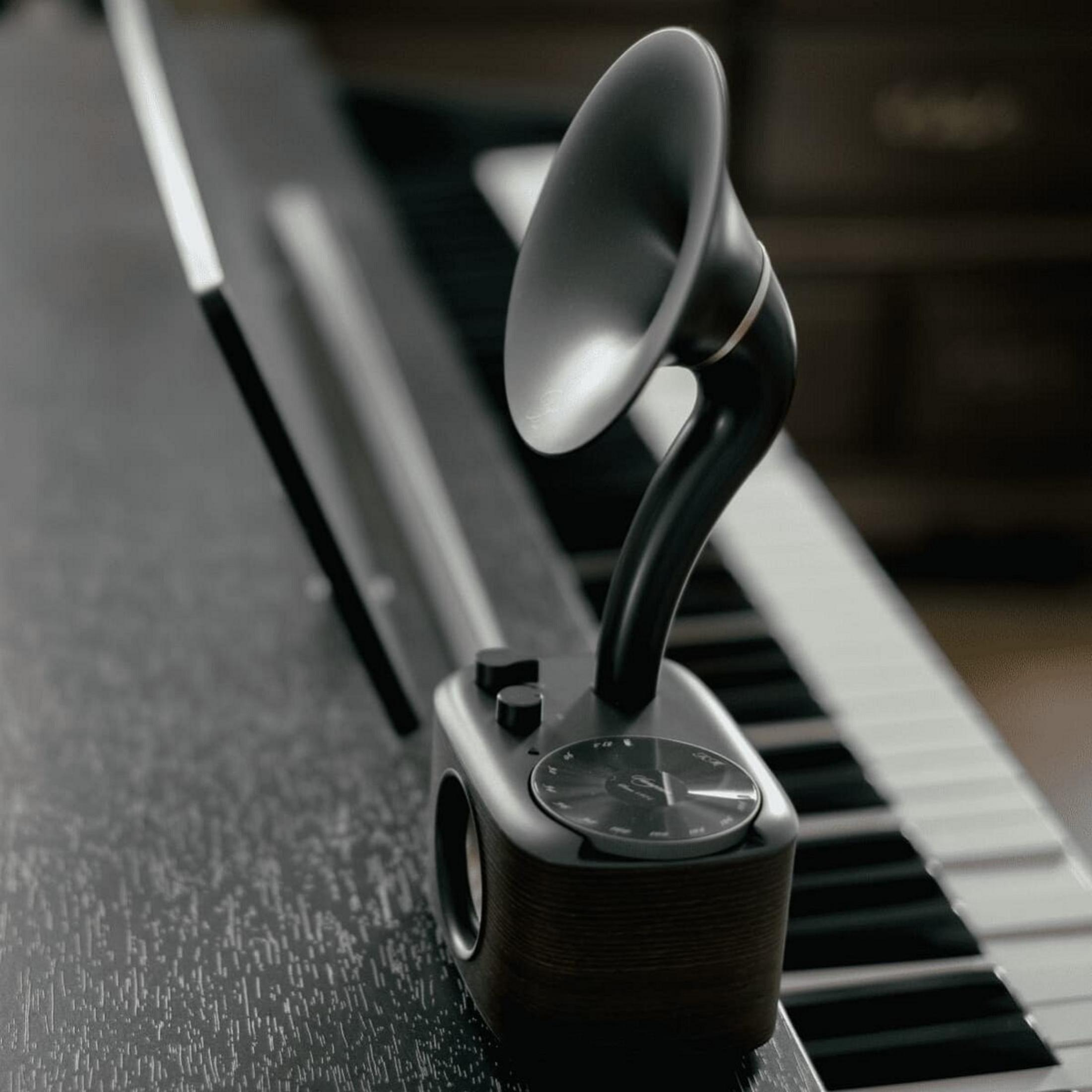 Un altavoz de estilo vintage con una bocina está sobre un piano. El altavoz es negro y marrón. Las teclas del piano están en el fondo.