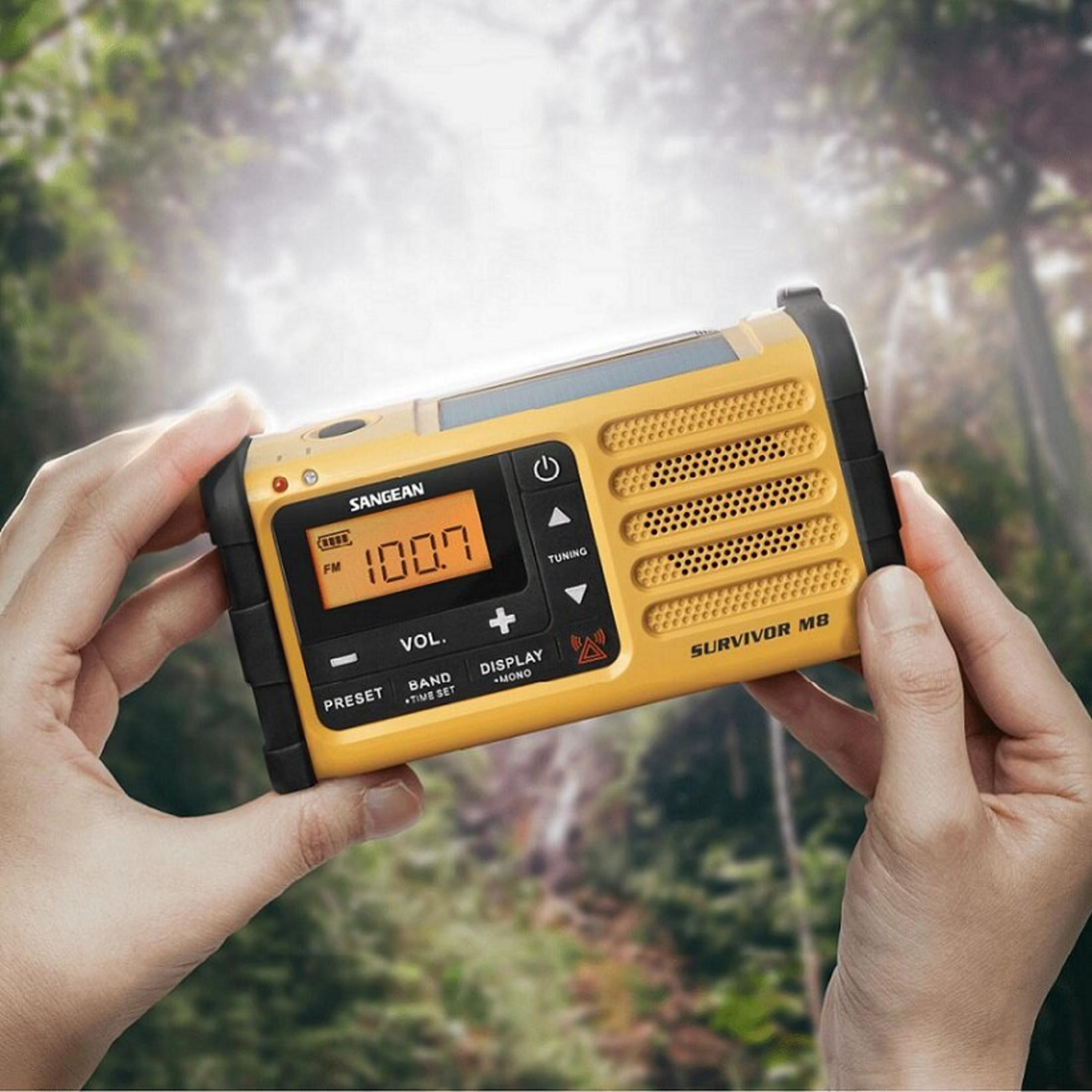 Una radio gialla, tenuta in mano, mostra '100.7'. Lo sfondo mostra una foresta.