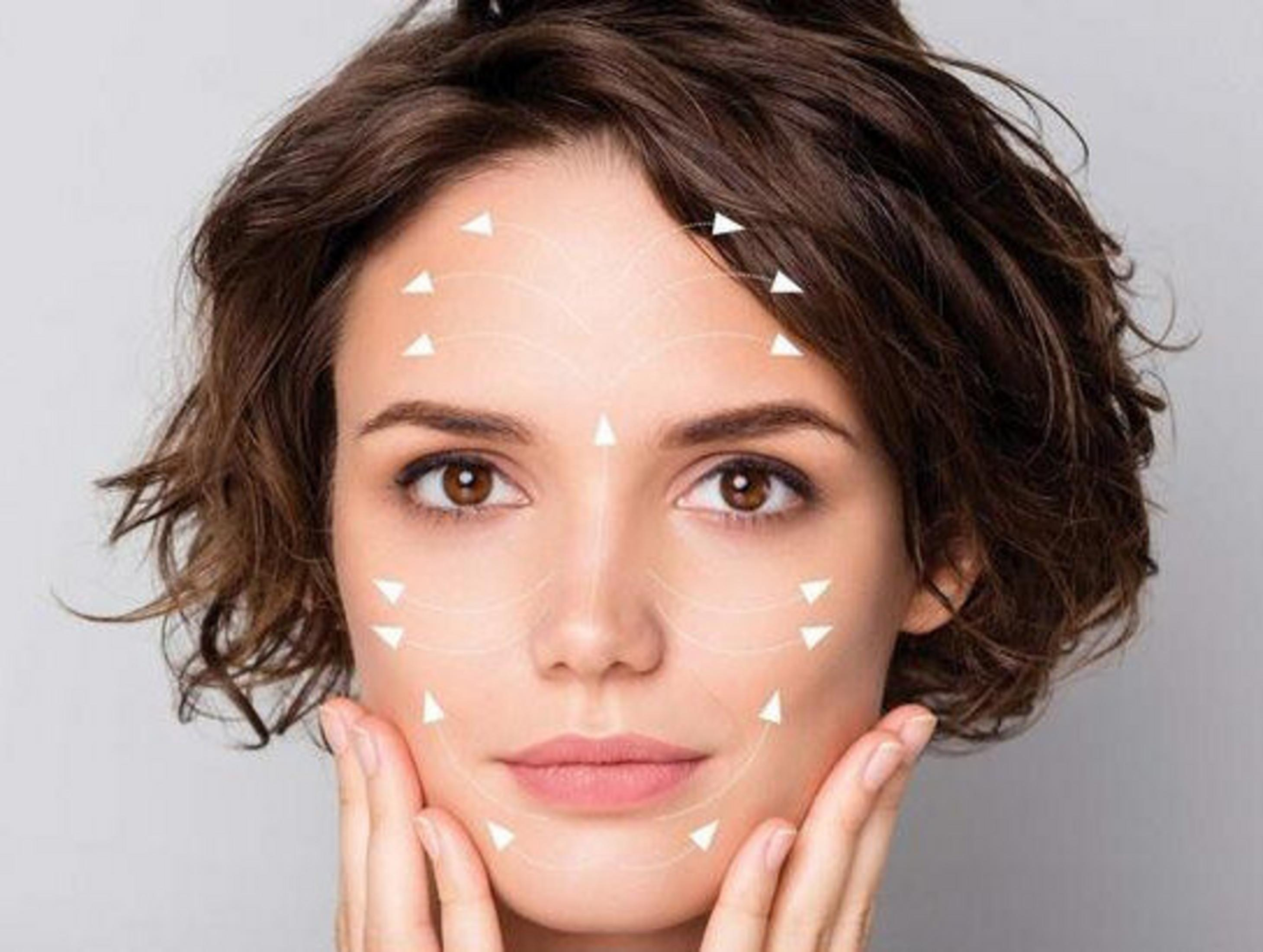 Twarz kobiety ze strzałkami wskazującymi punkty liftingu. Ma brązowe włosy, oczy i dotyka twarzy.