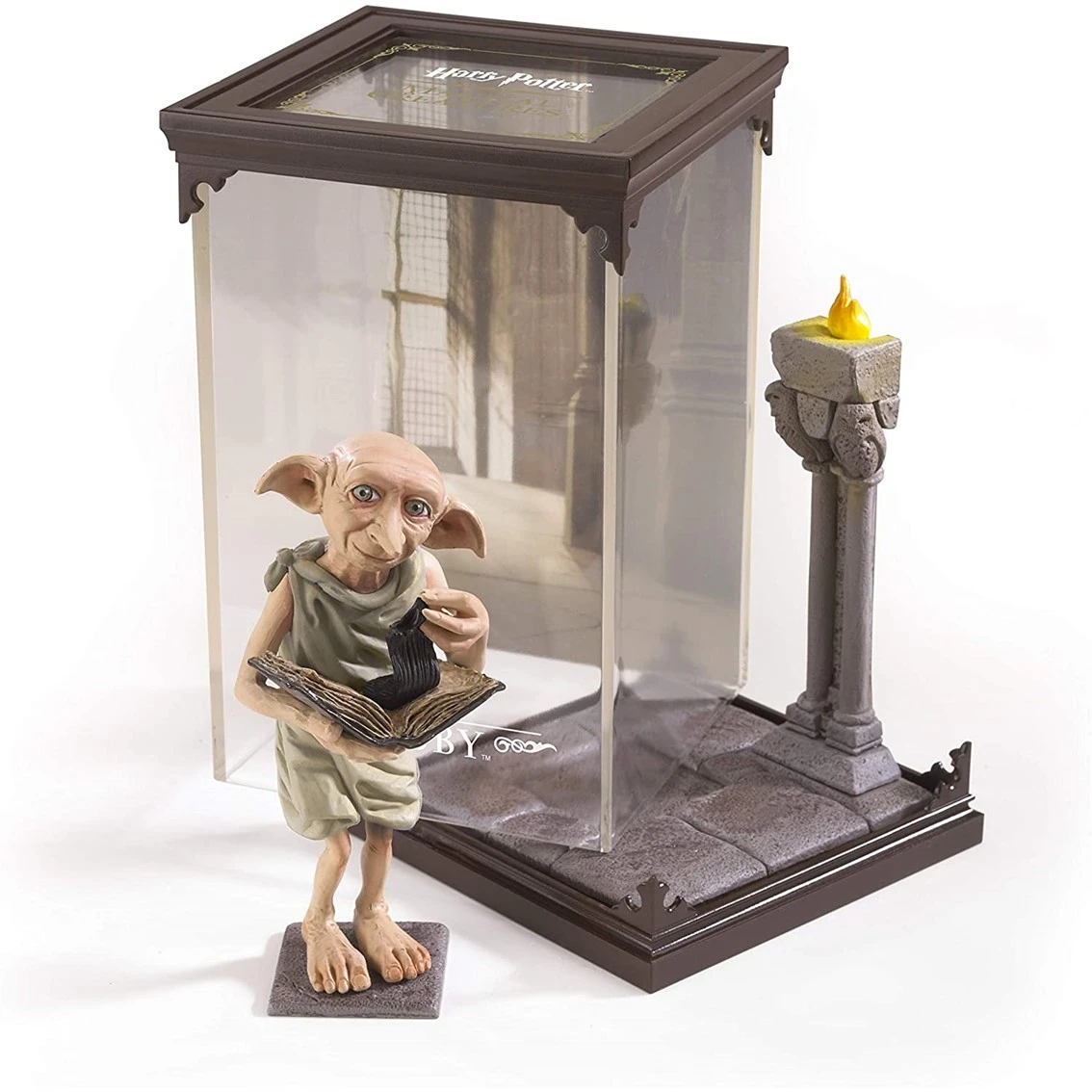 Una figura de Dobby sostiene un libro y un calcetín dentro de una vitrina, junto a una pequeña columna con una llama amarilla.
