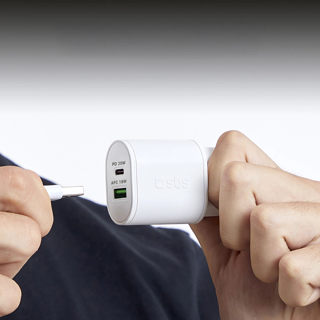 Una persona tiene in mano un caricabatterie bianco e un cavo bianco. Il caricabatterie ha le etichette: PD 20W, AFC 18W. Lo sfondo è bianco.