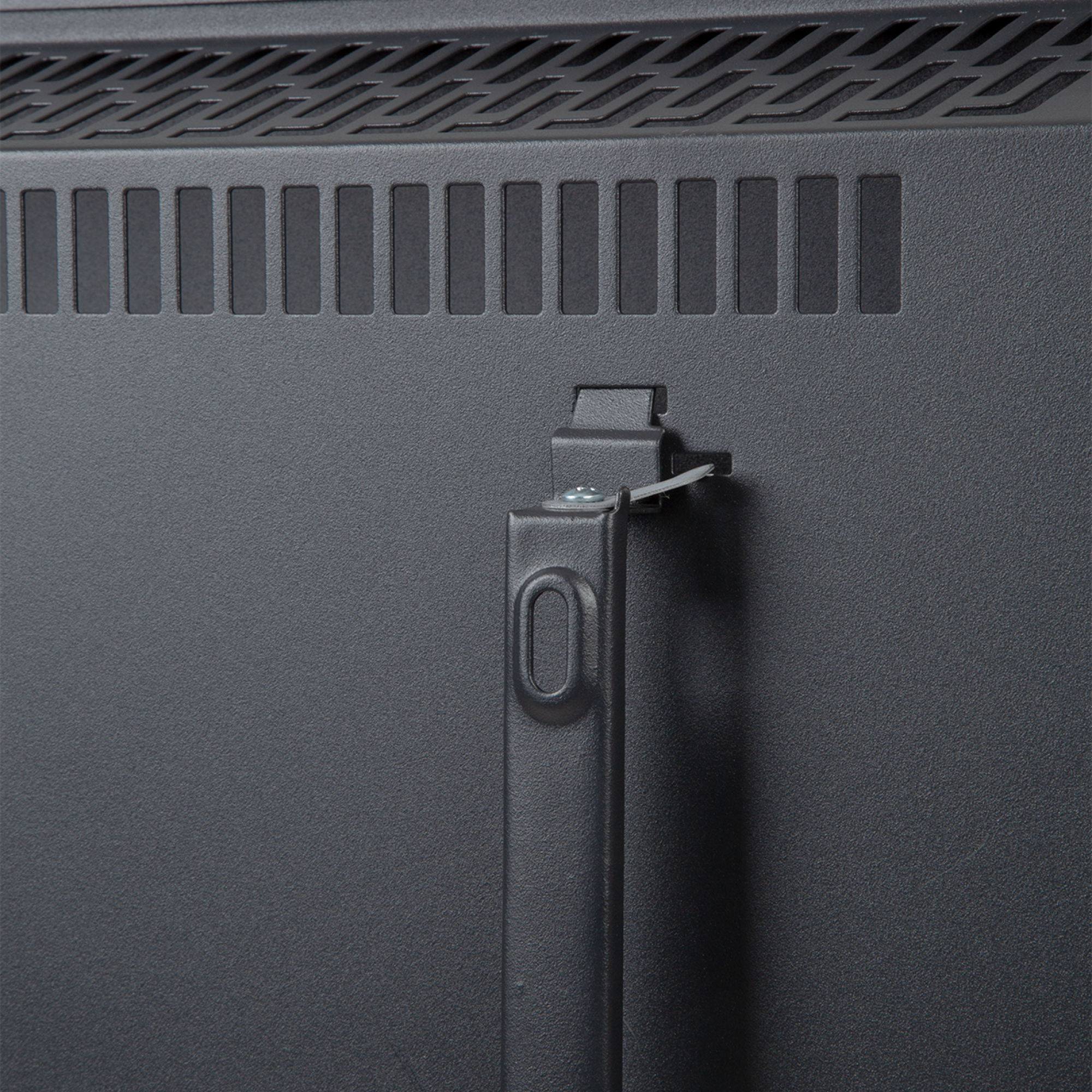 Primer plano de un panel metálico gris oscuro con ranuras de ventilación y un asa. Un soporte metálico sujeta una brida de plástico.