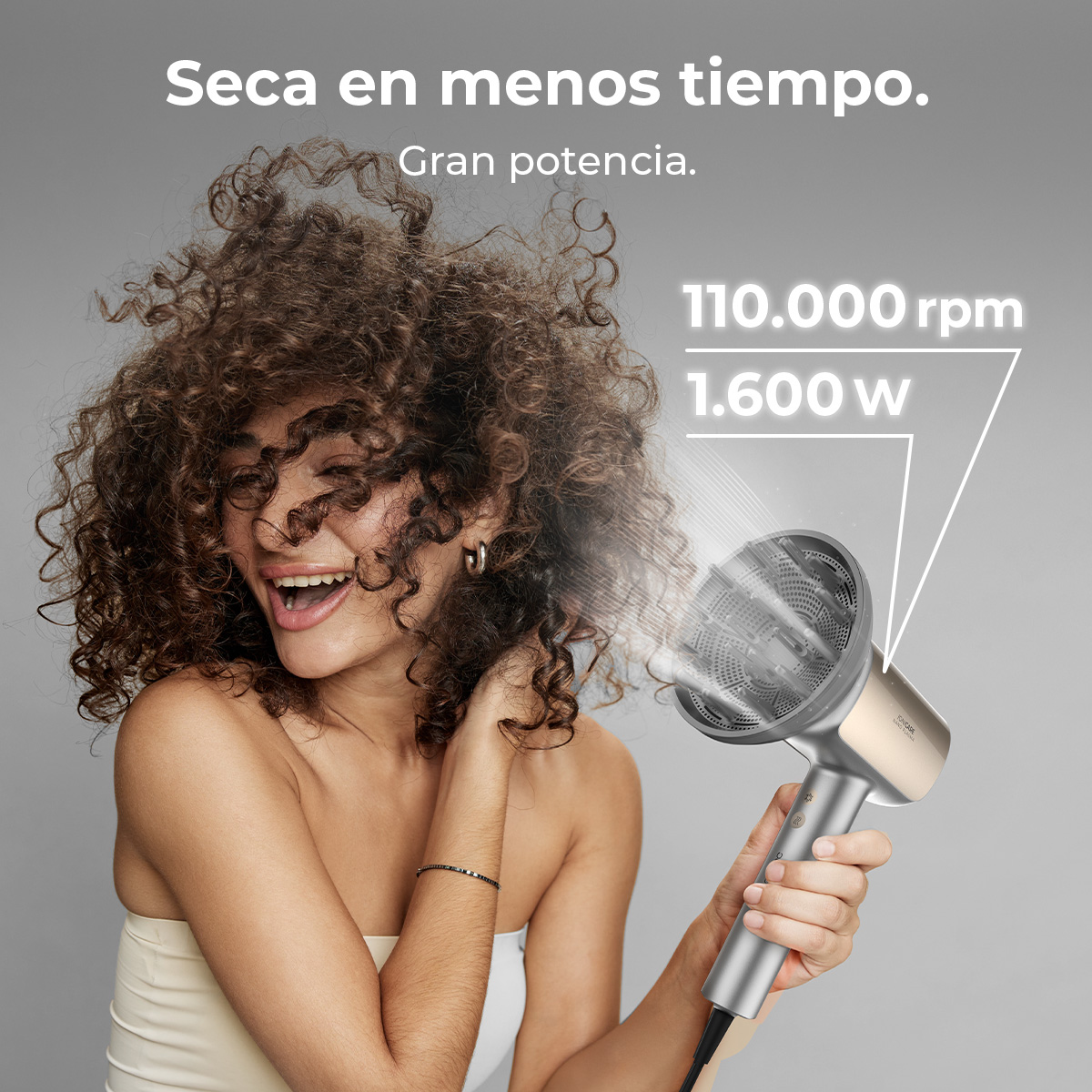 Una donna sorride usando un asciugacapelli. Il testo dice: Seca en menos tiempo. Gran potencia. 110.000 rpm 1.600 w.